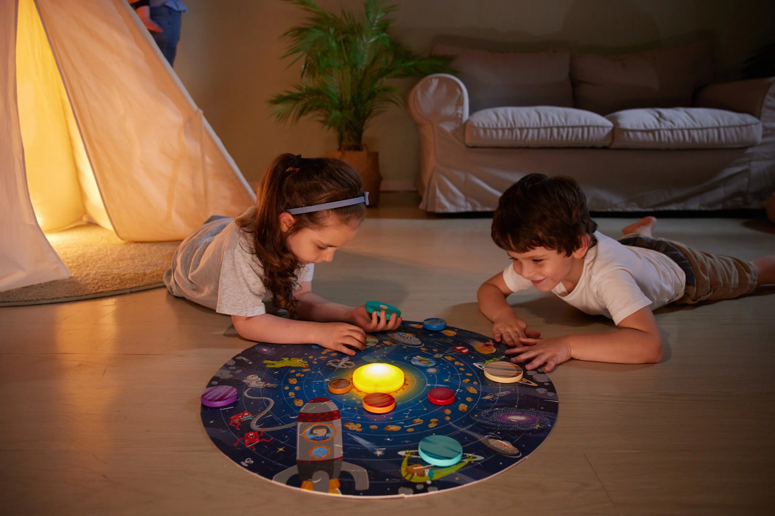 Two children lying on the floor playing with a Hape space-themed puzzles in a cozy living room.