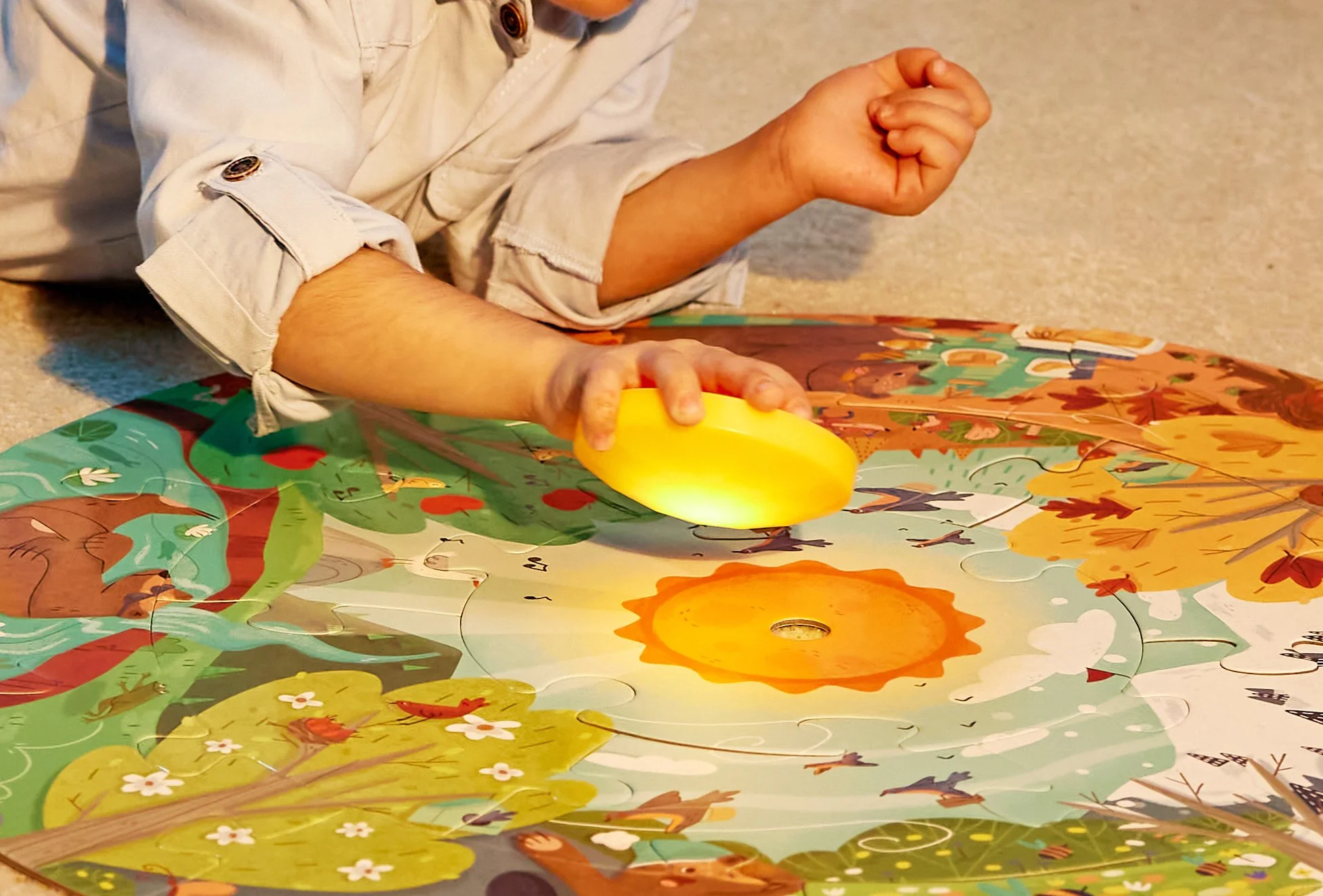 Child playing with a bright sun on a colorful illustrated Hape puzzle themed seasons.