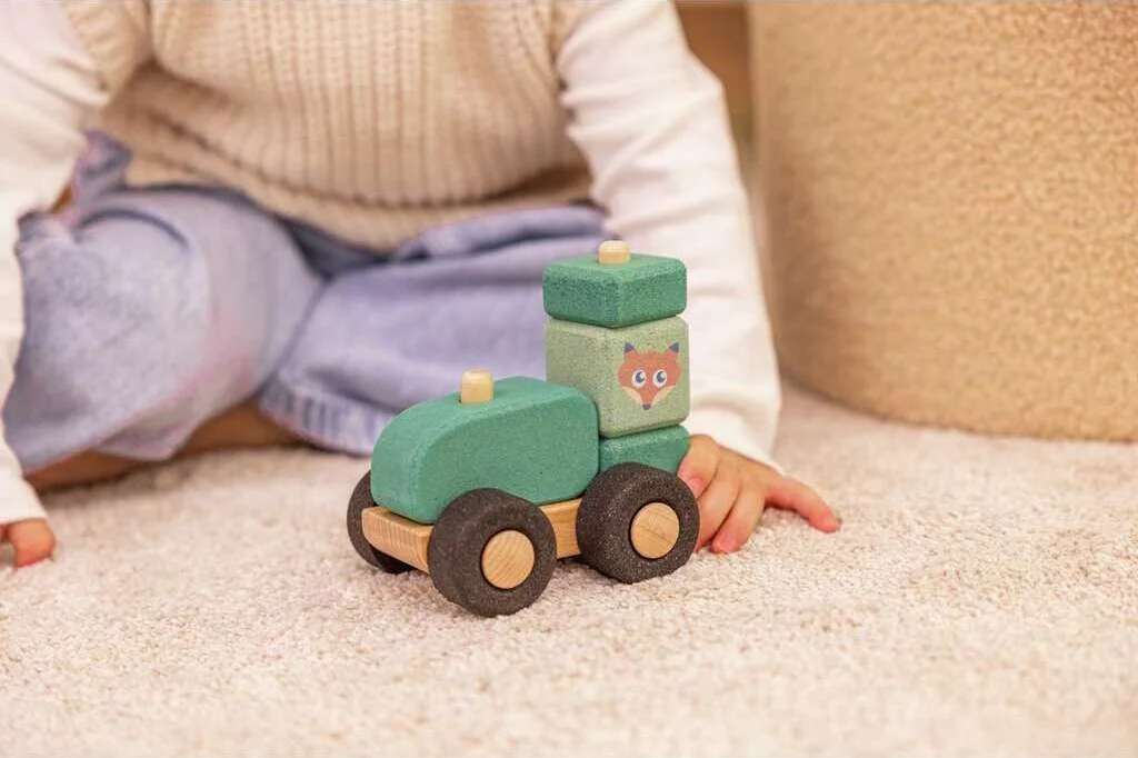 Child playing with a toy train made of wood and green cork with a graphic of a fox on a beige carpet. By Korko.