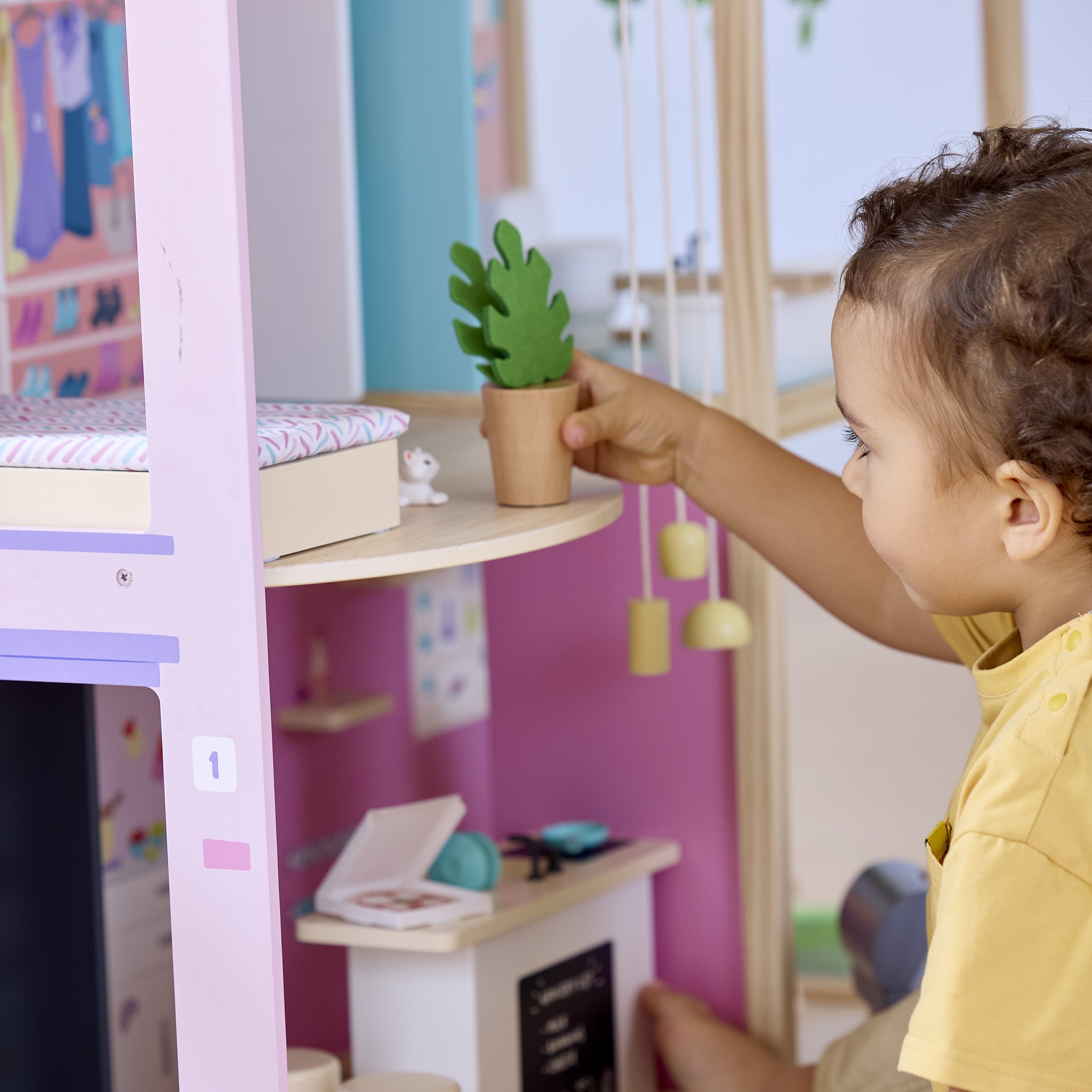 A young child playing with a toy potted plant inside a colorful play kitchen.