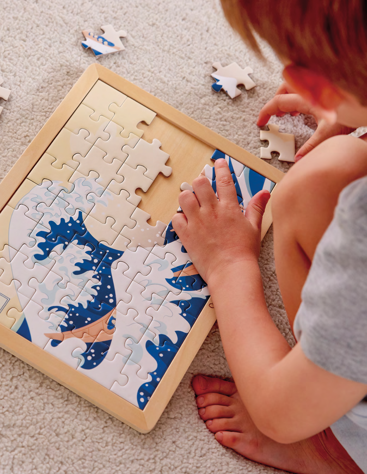 Child assembling an Hokusai Great Wave Puzzle jigsaw puzzle branded Hape in collaboration with the MET Museum