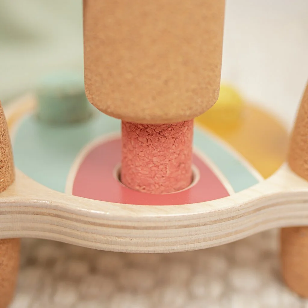 Close-up of a colorful wooden and cork children's toy with a pink pillar, surrounded by pastel-colored circular parts. By Korko.