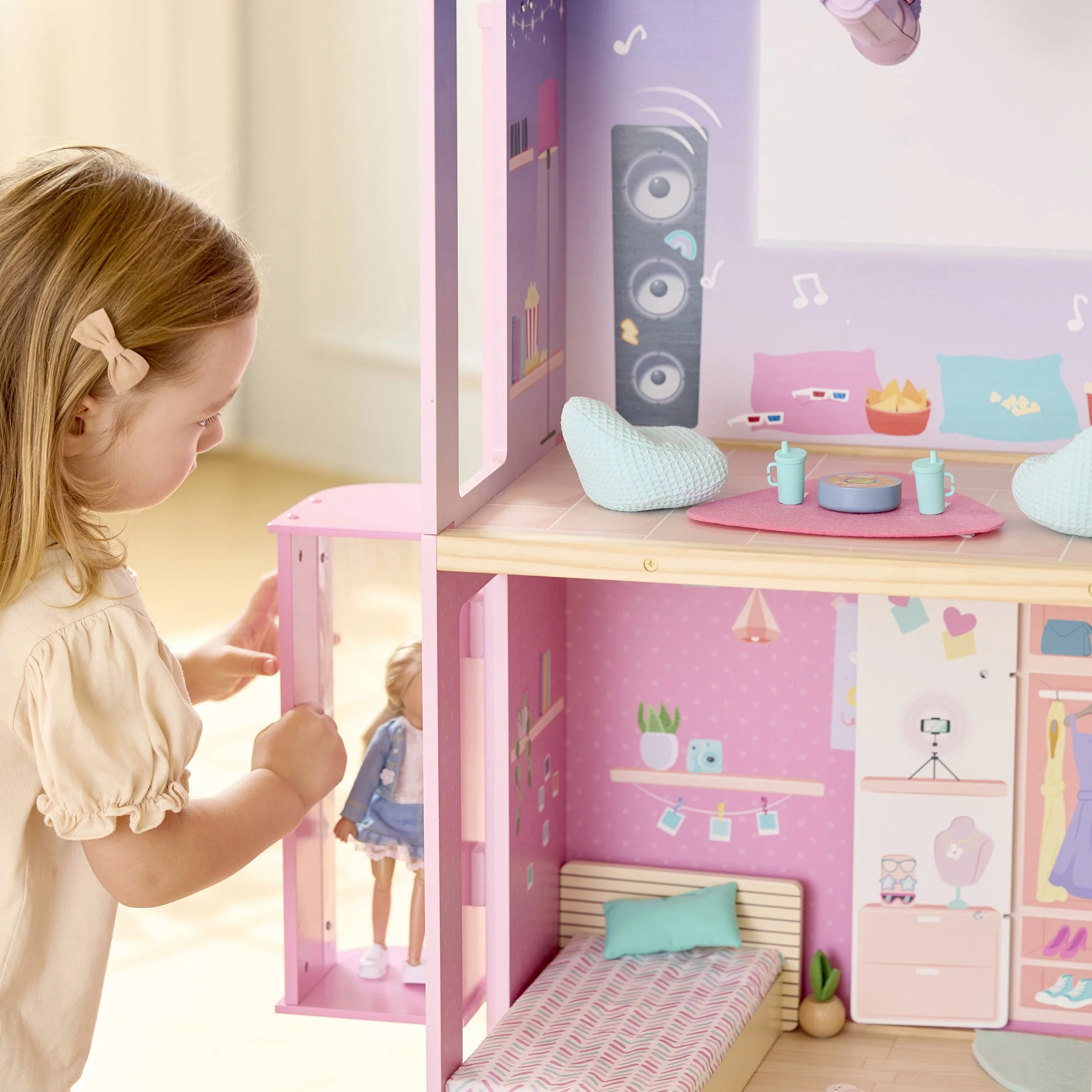 A young girl playing with a pink dollhouse, which has different rooms and miniature furniture.