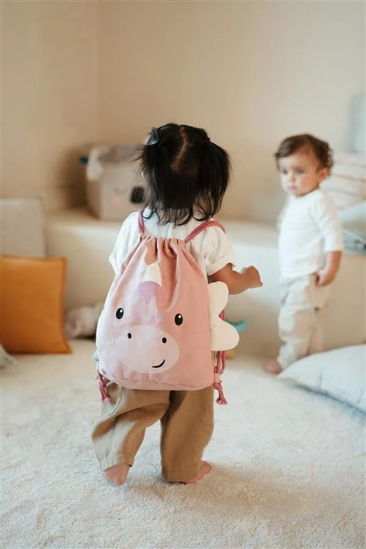 Two young children in a cozy bedroom, one with a pink backpack featuring a smiling animal face, and the other standing near a bed.