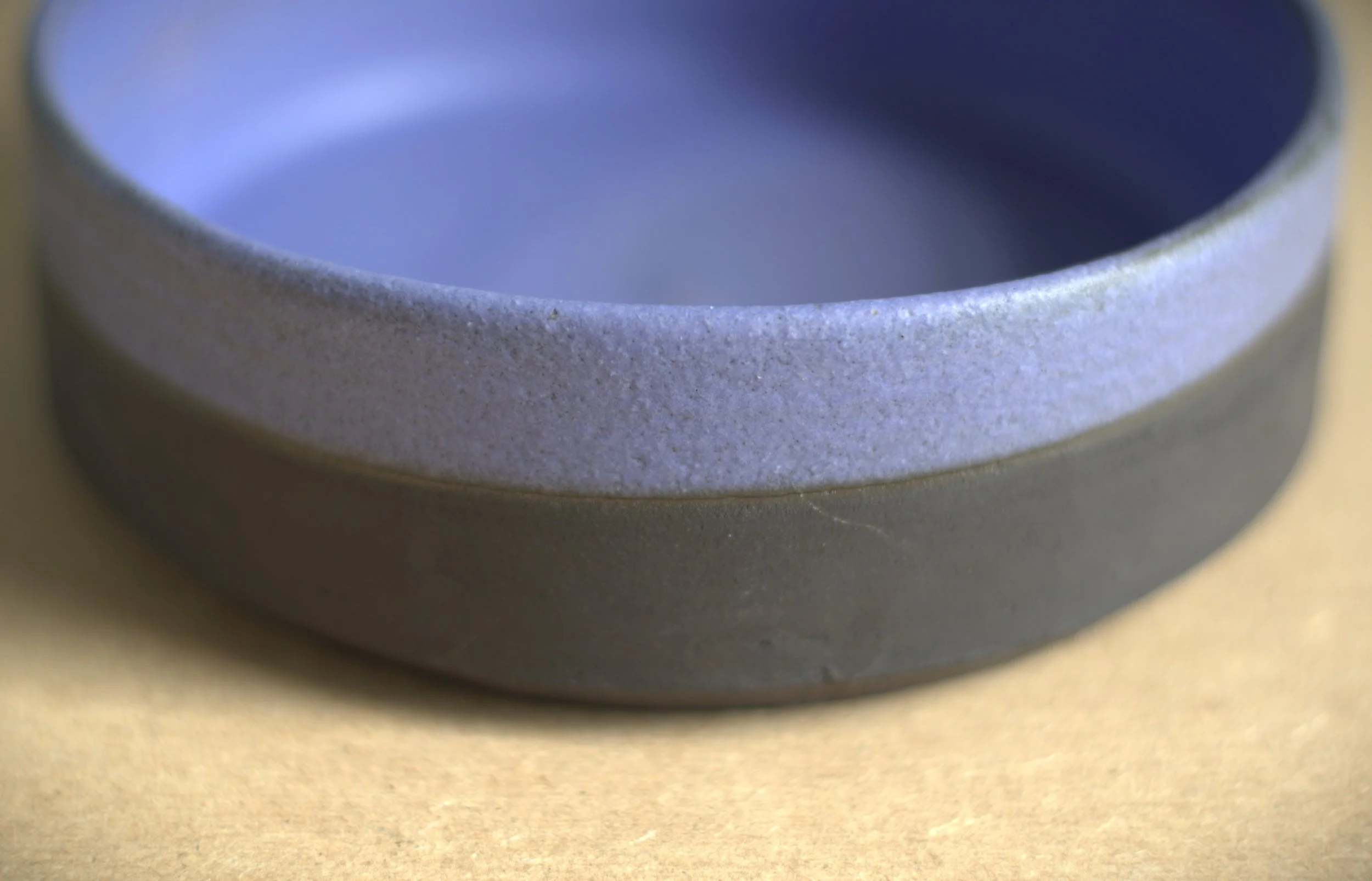 Close-up of a ceramic bowl with a textured, gray exterior and a smooth, blue interior on a beige surface.