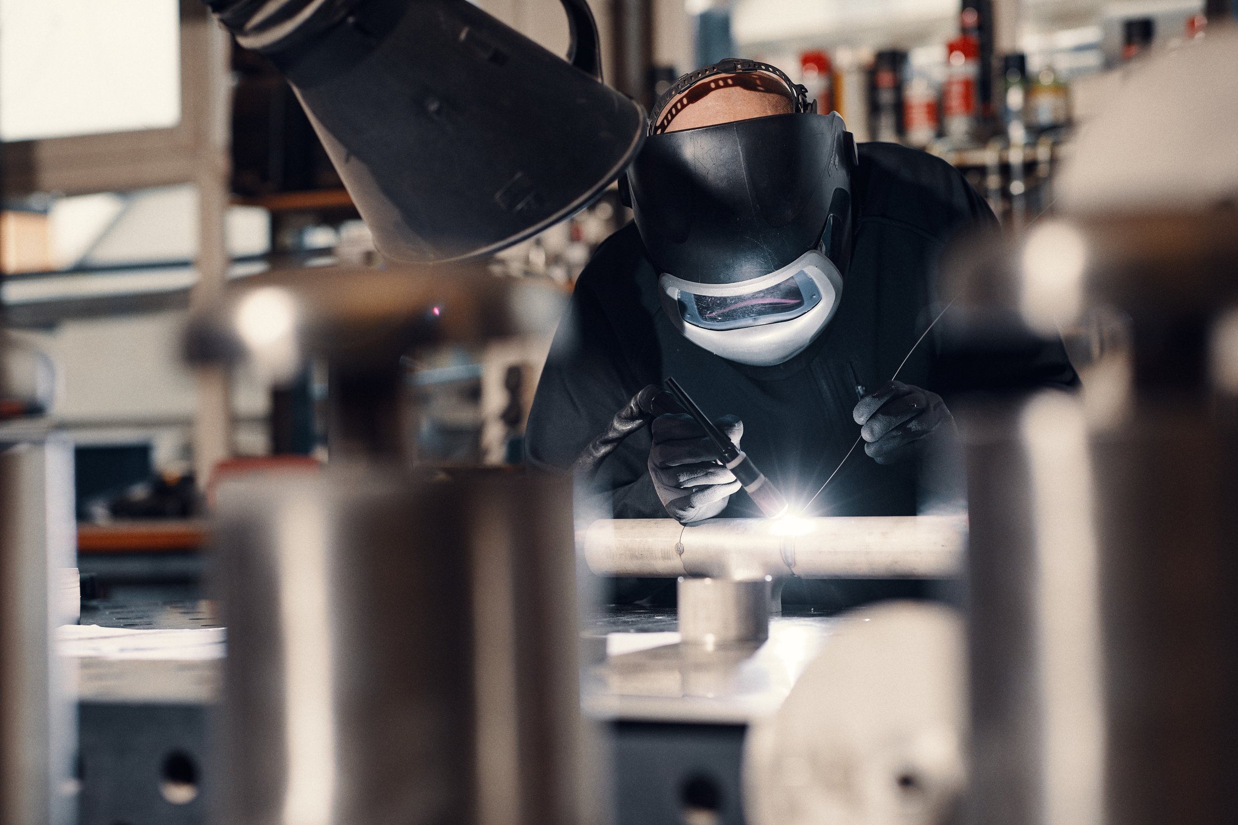 Männer beim Schweißen in einer Werkstatt, trägt Schutzhelm und -maske, um in einem industriellen Umfeld zu arbeiten.