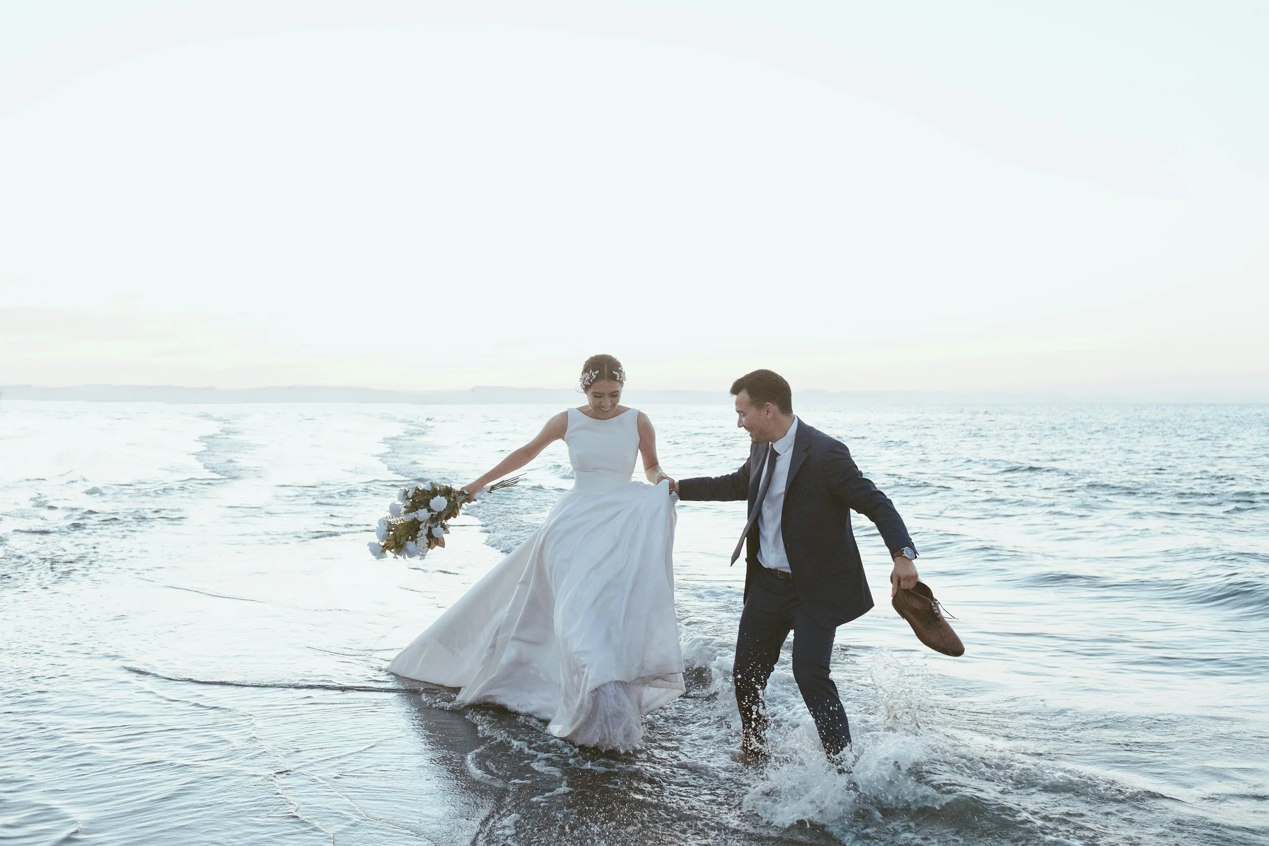 bride and groom holding hands laughing in the sea