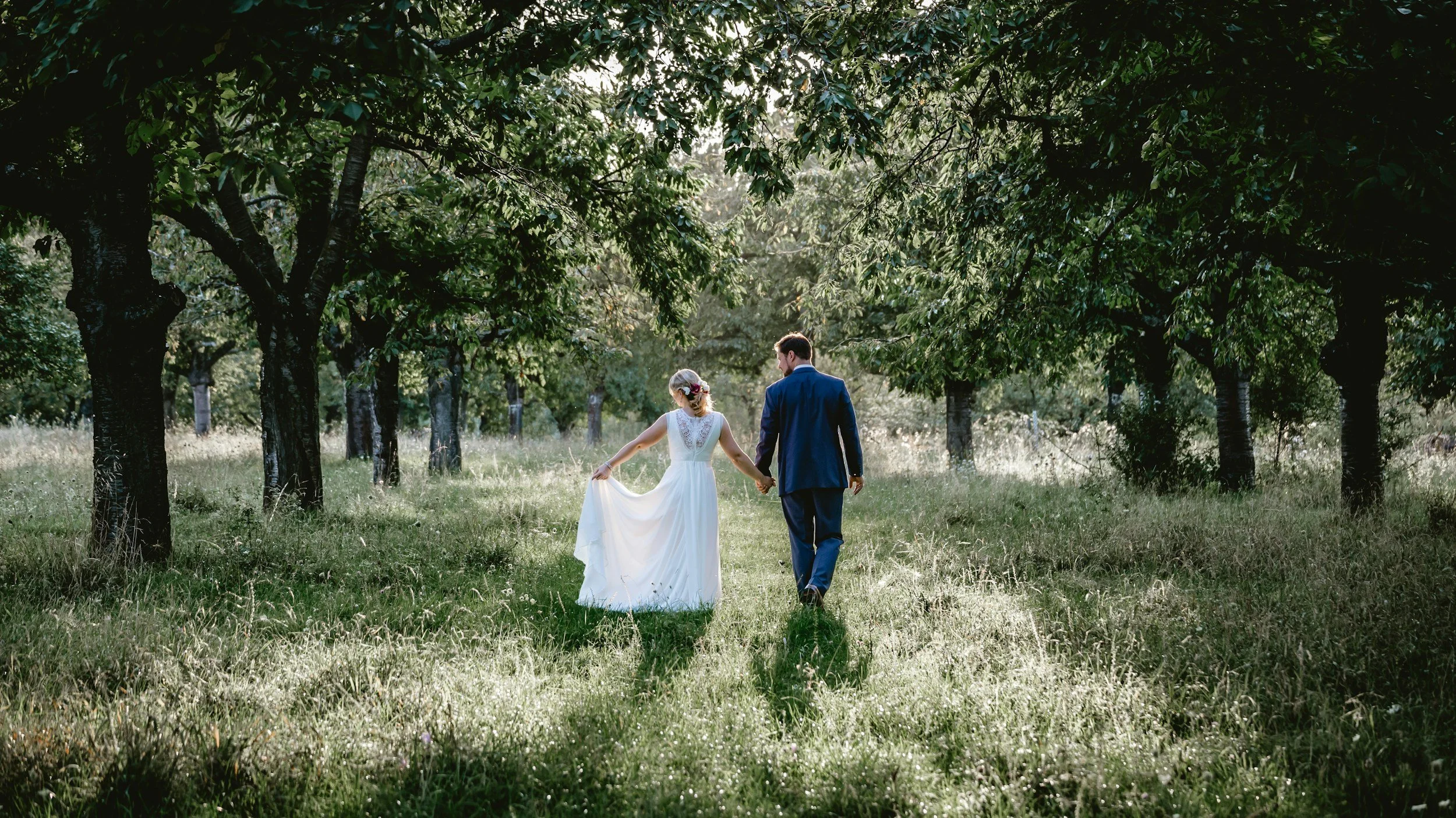 bride and groom holding hands walking away in orchard