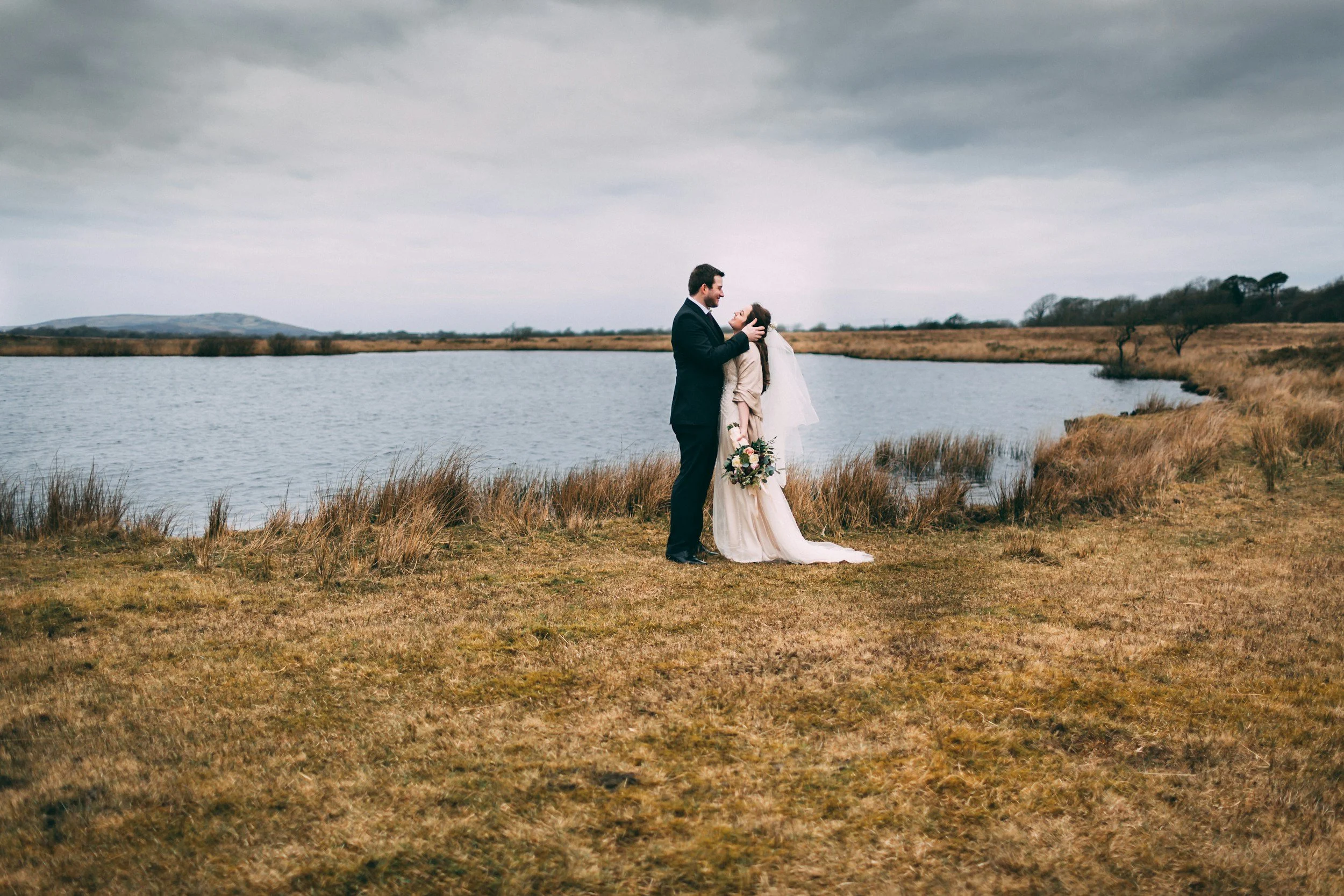 bride and groom together stood on the edge on a lake