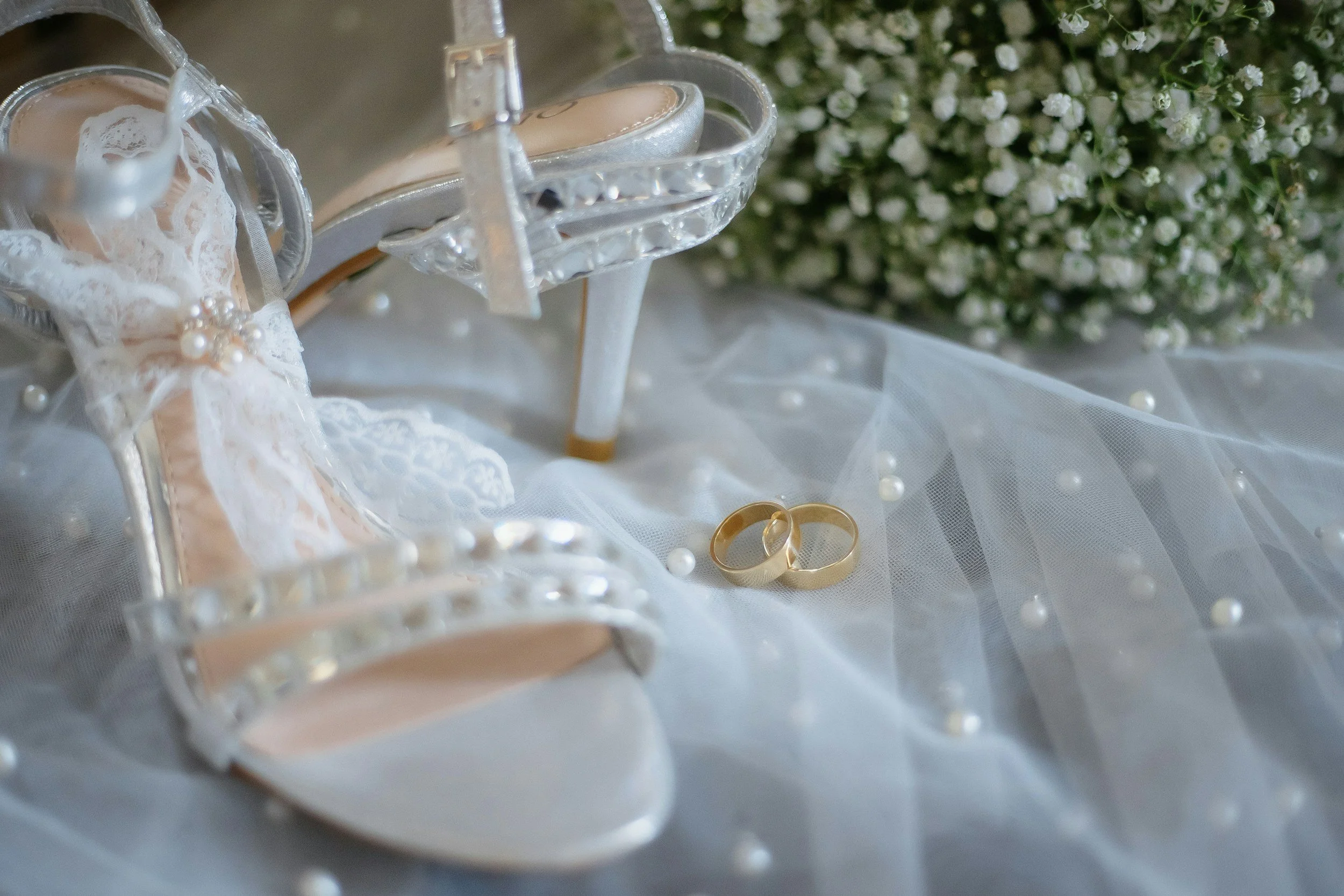 white wedding shoes on lace with wedding rings and white flowers