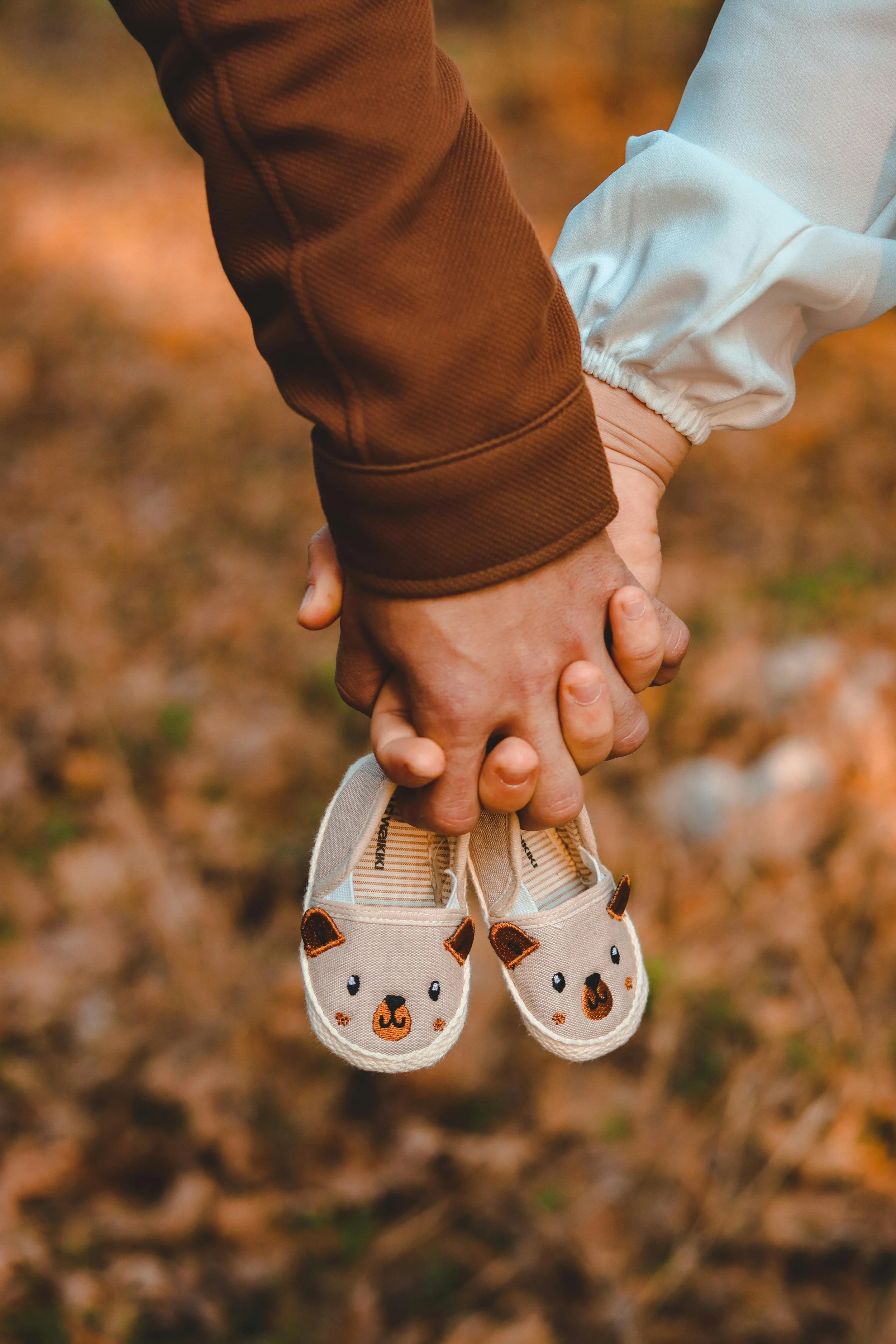 expecting parents holding hands with baby shoes