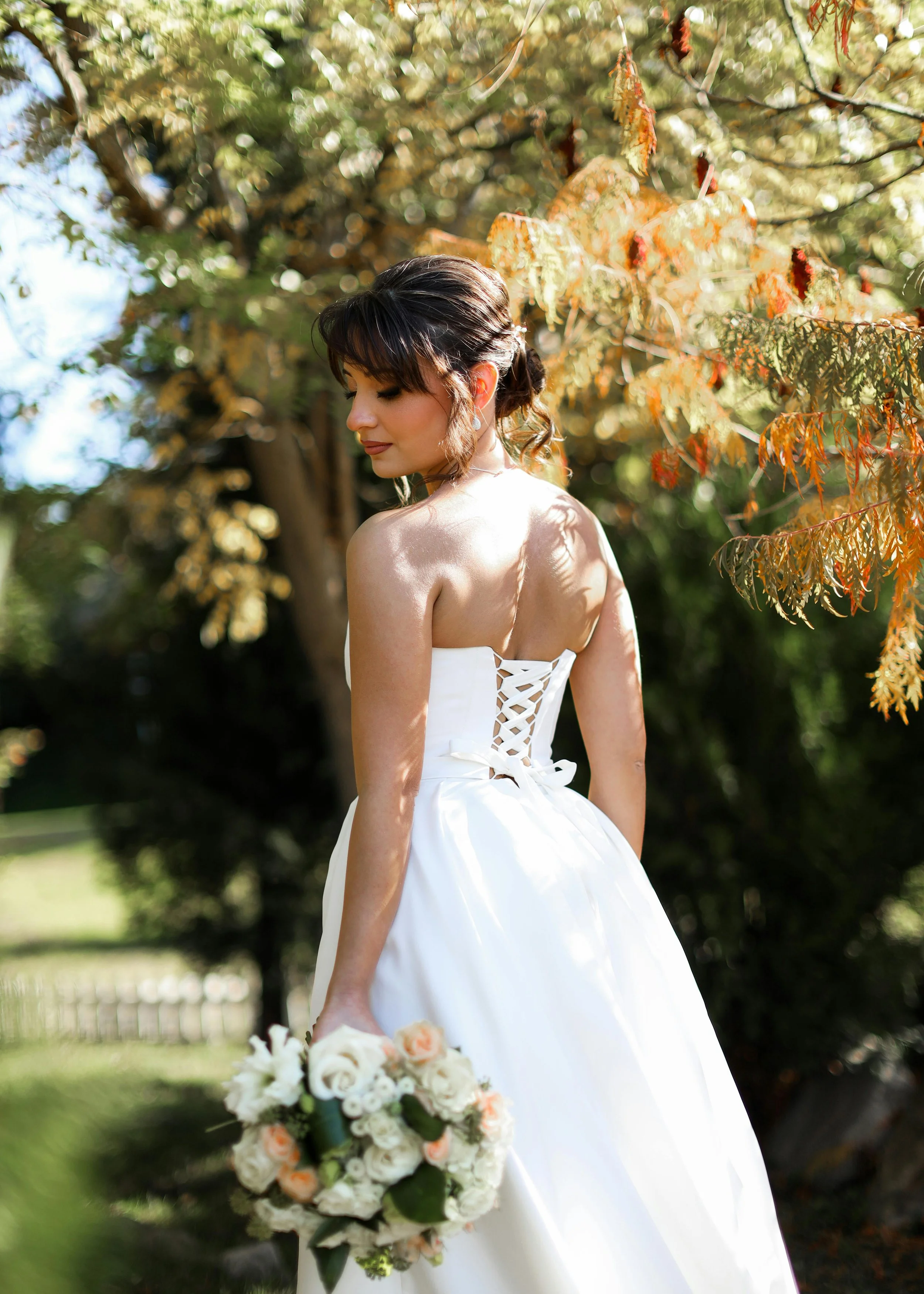 Bride on her own walking the garden with the sun on her back with her wedding bouquet in hand