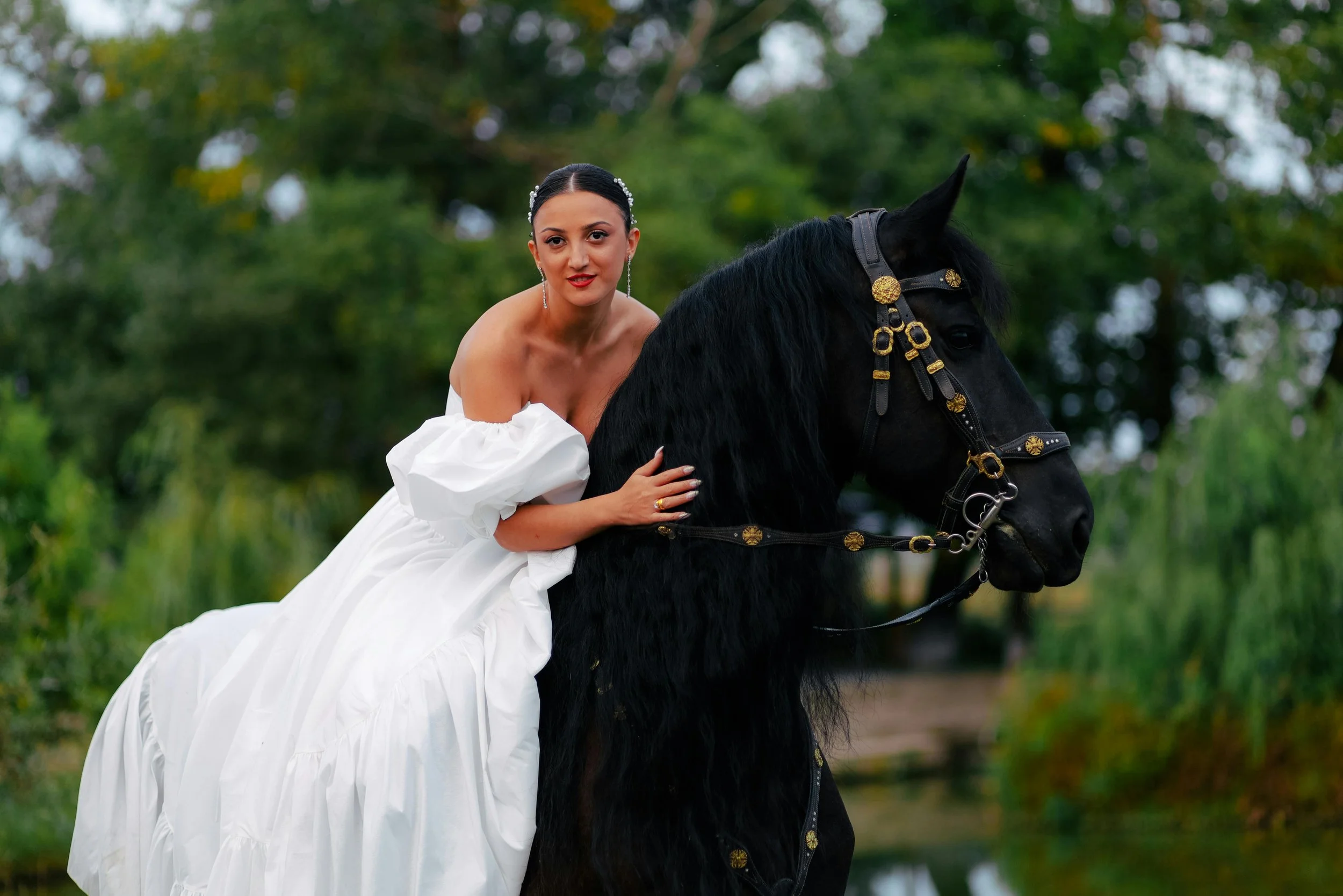 bride sat on her black Friesian leaning forward looking at the camera whilst her horse is looking away