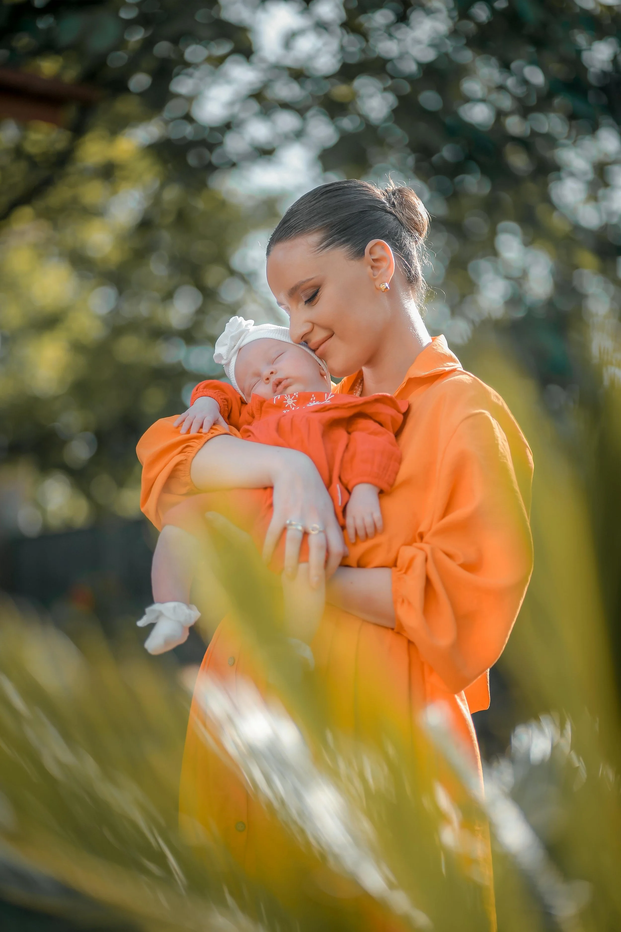 mother holding her new born baby in bright orange dress looking at her baby lovingly