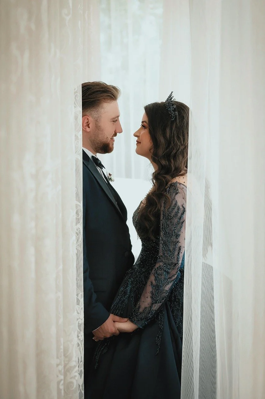 bride in black wedding dress holding hands with the groom in window