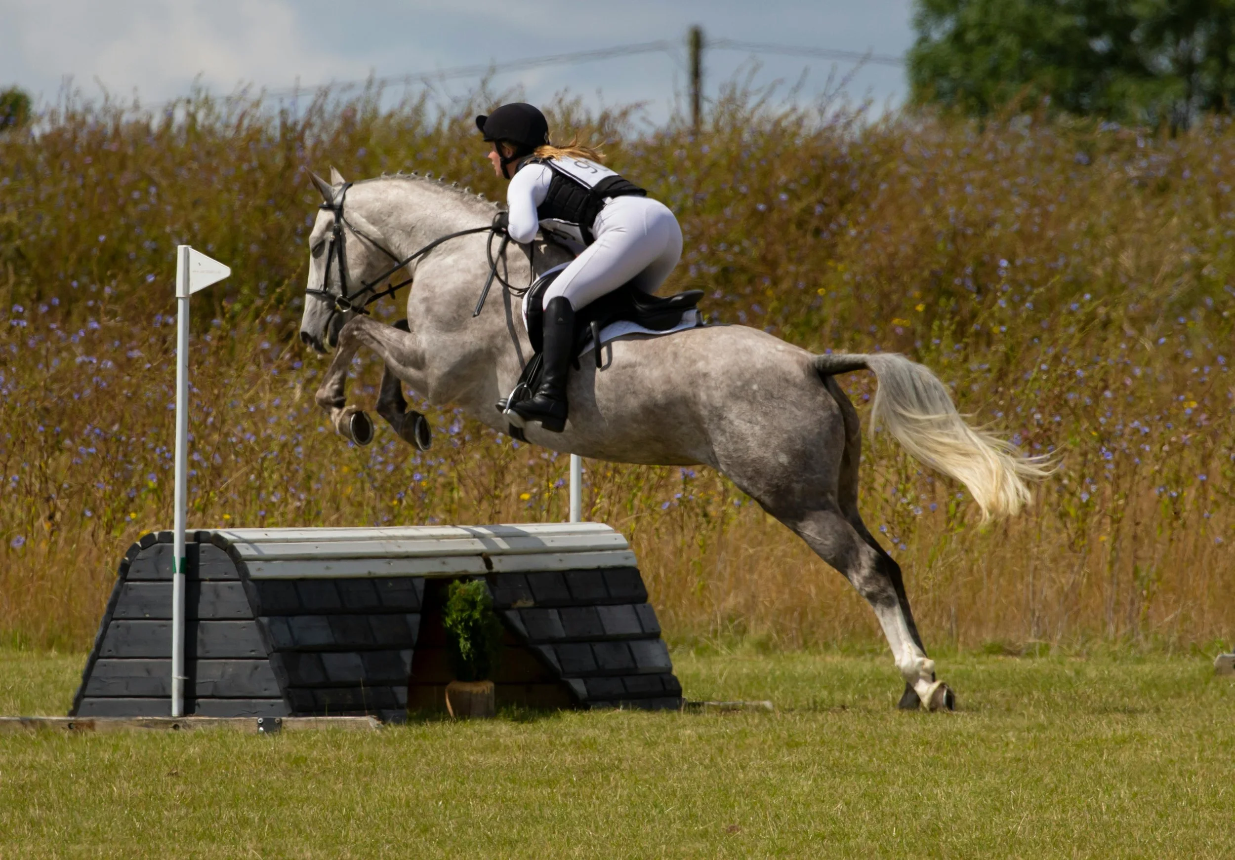 grey horse with rider going over cross country jumps