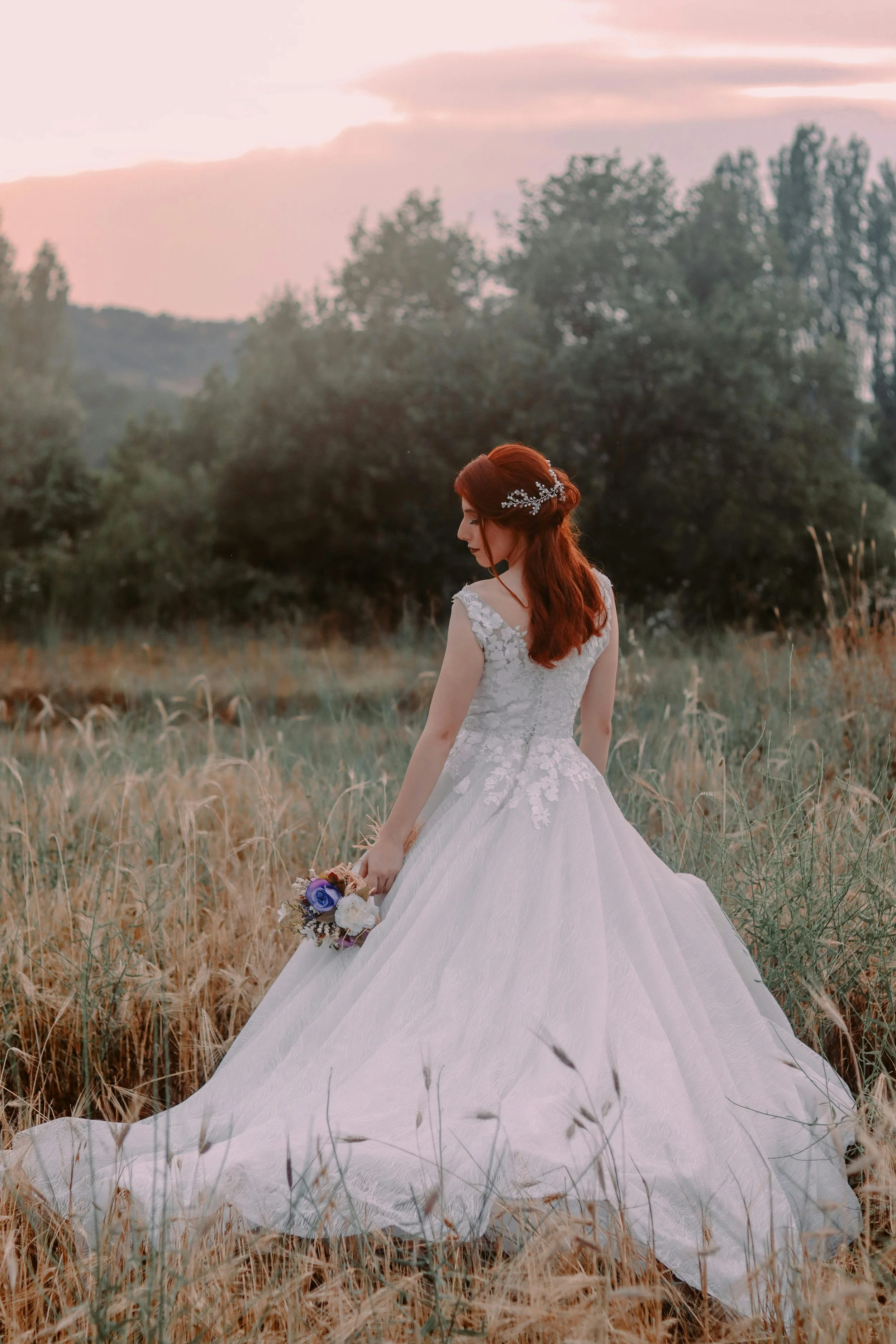 bride in open field looking down at the floor with back turned to camera