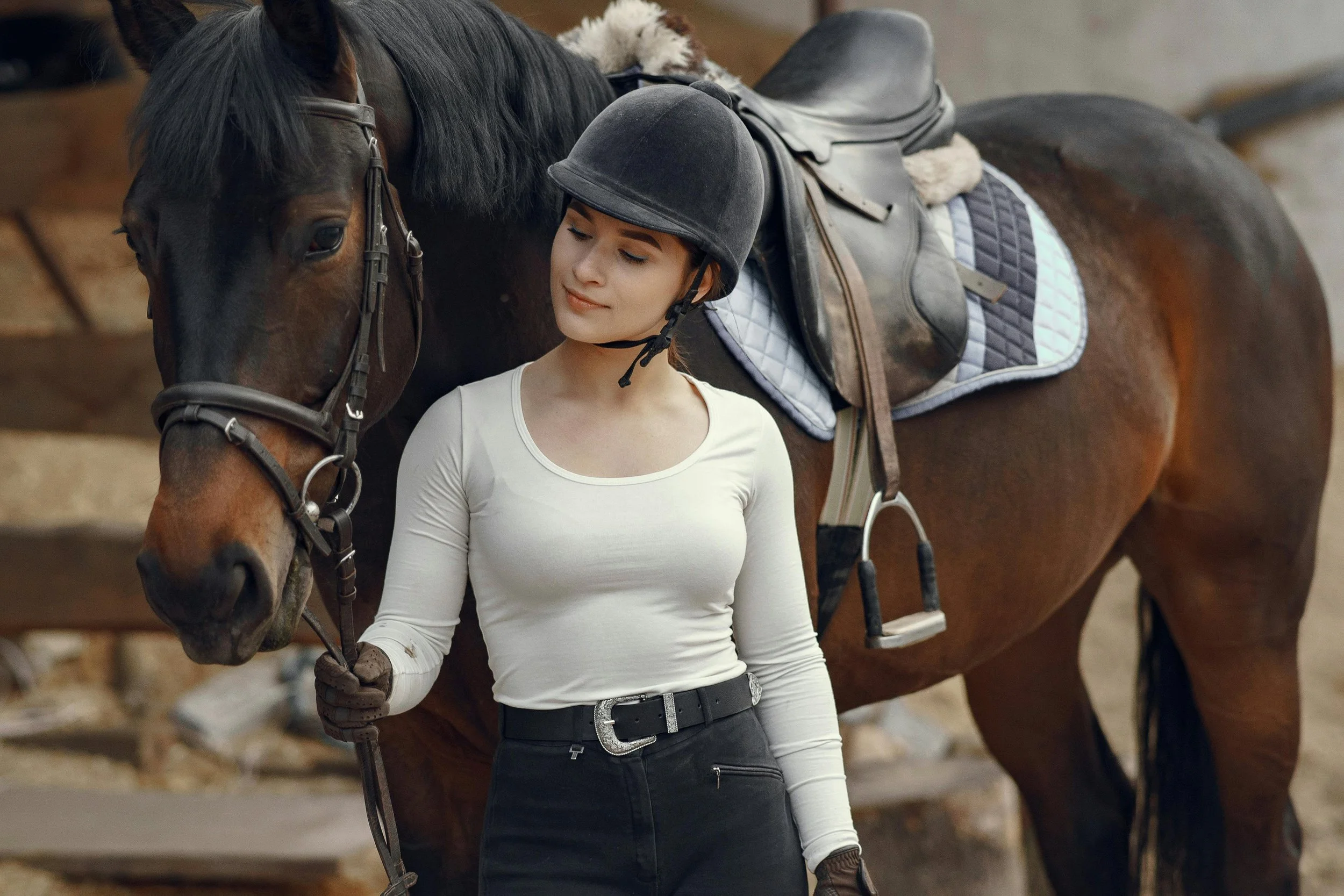 girl and her horse stood together looking at her horse with riding hat on ready to ride