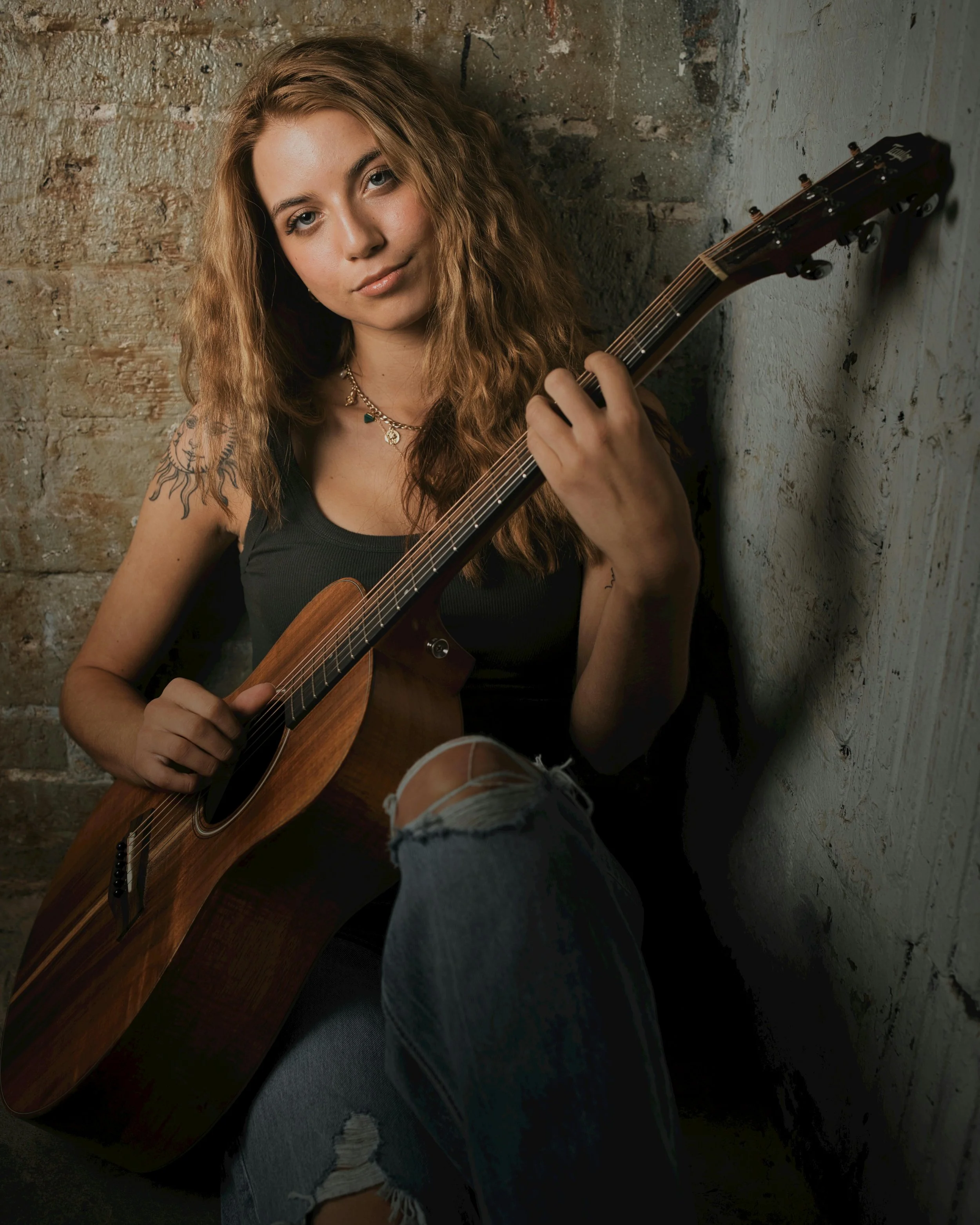 female singer leaning up against concrete wall with guitar