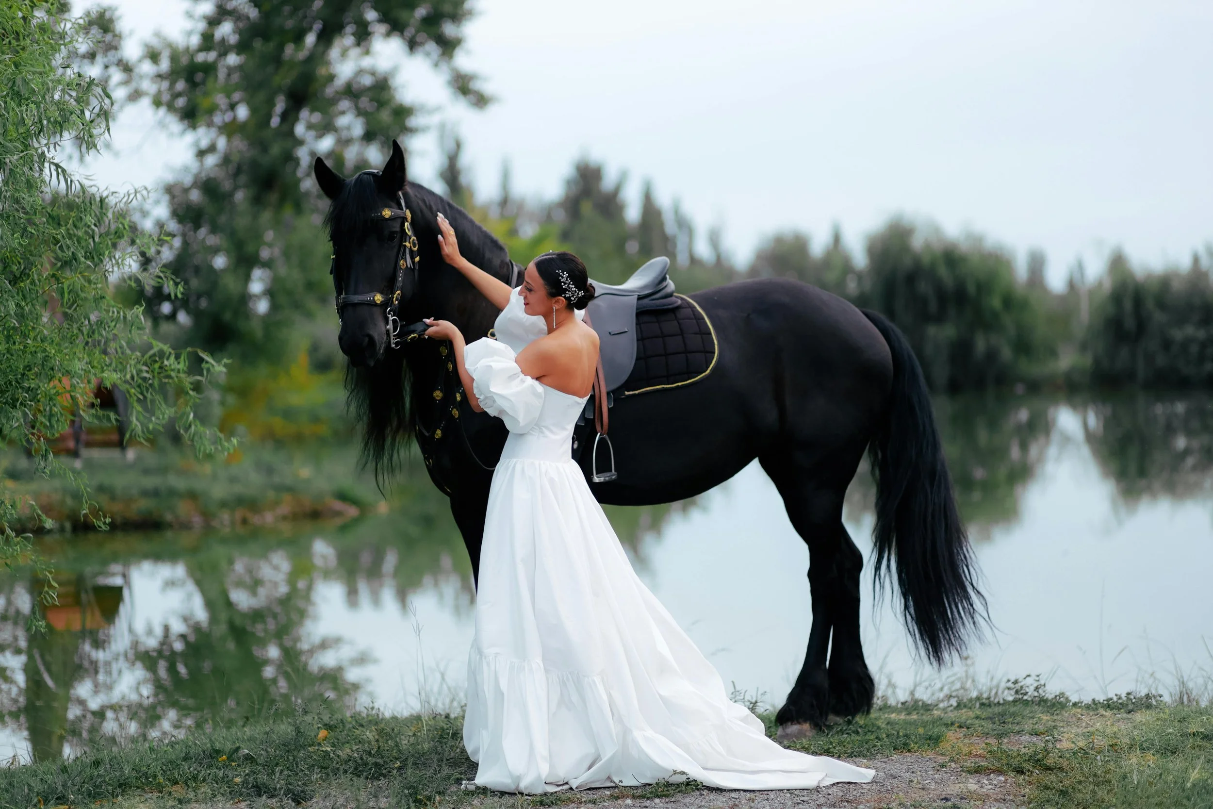 bride with her black Friesian stallion stood next to a lake