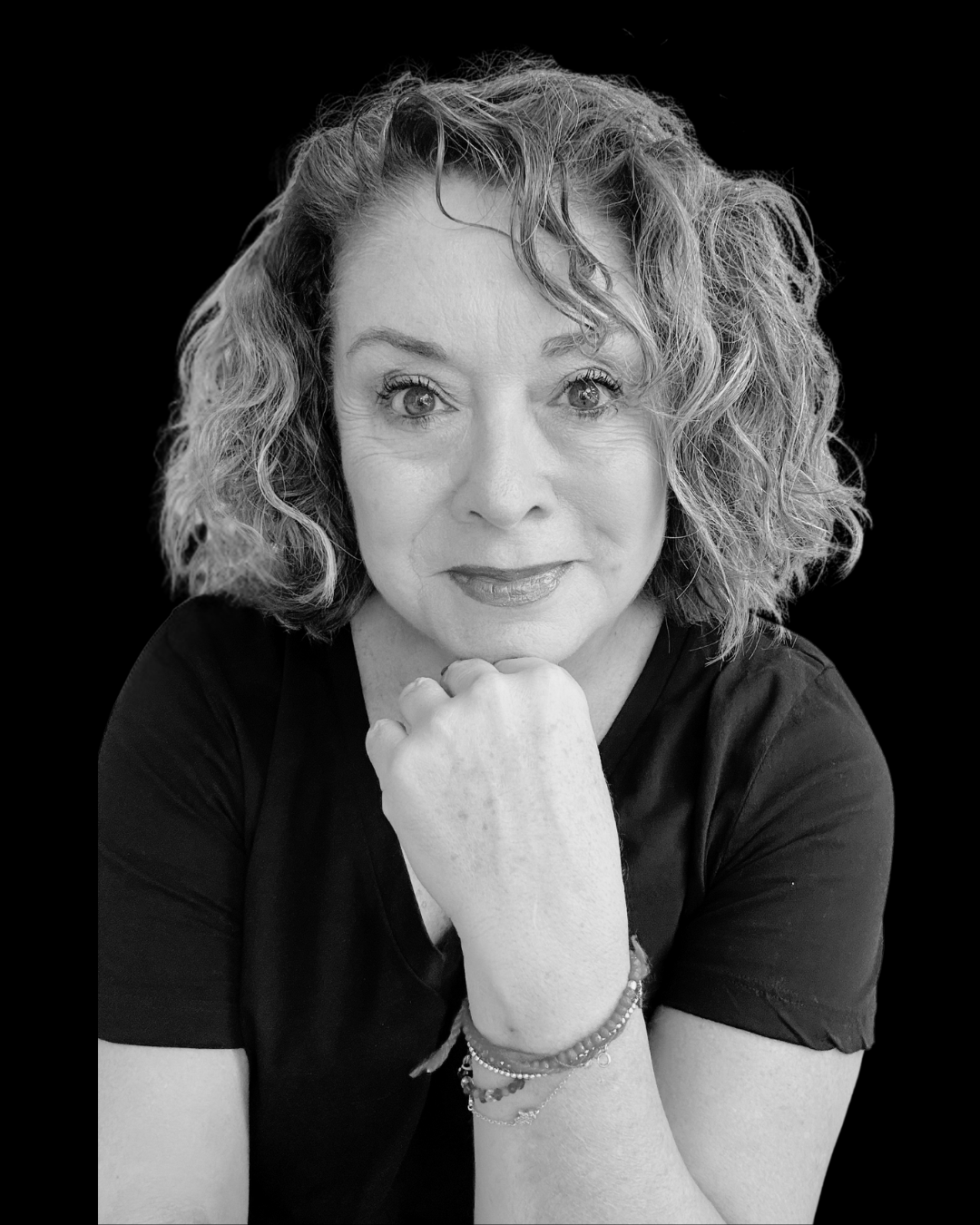 Retrato en blanco y negro de una mujer con cabello rizado y mirada directa, apoyando su barbilla en su mano, con fondo negro.