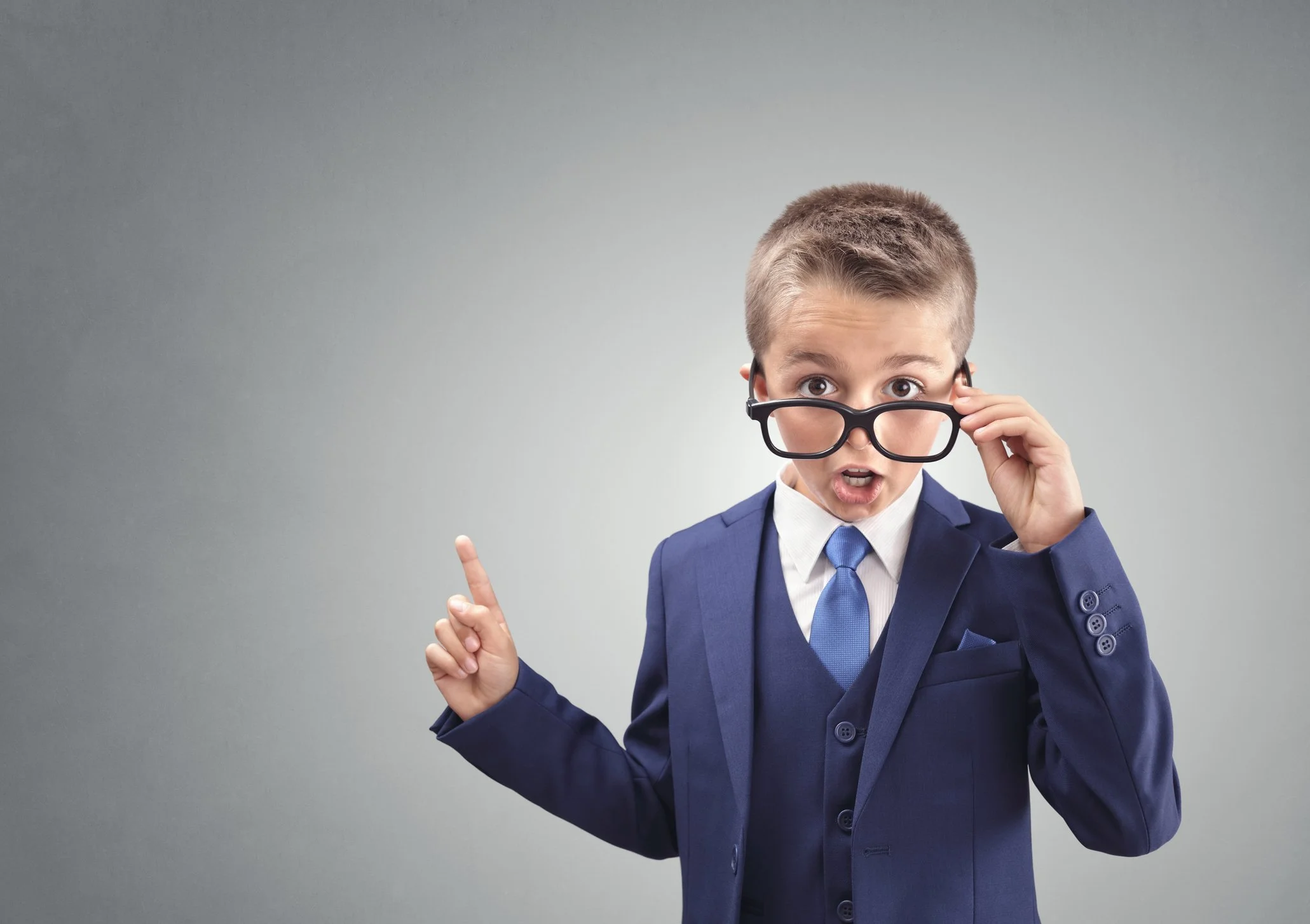 Boy in suit wearing glasses poiting upwards