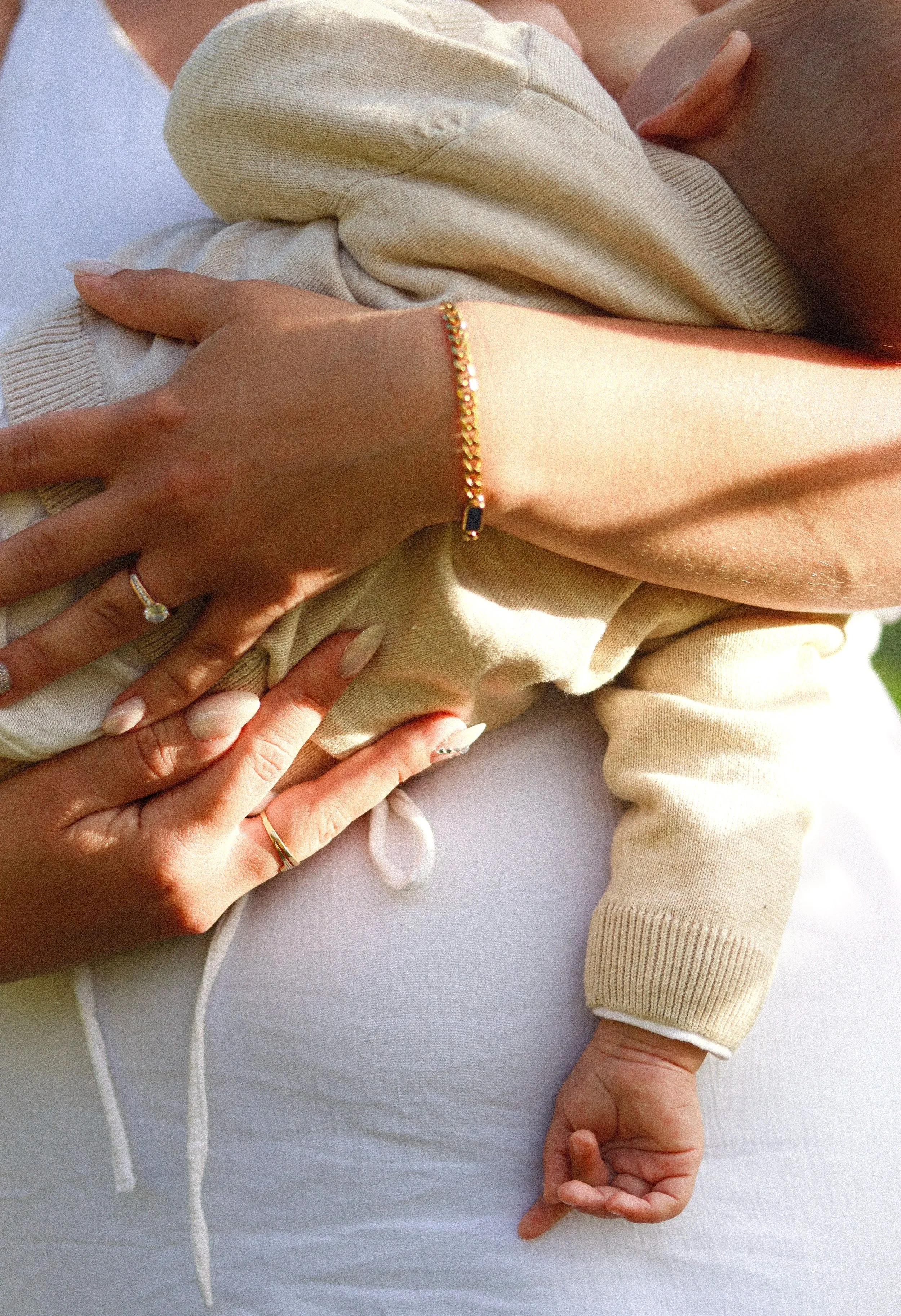 Une mère tenant un bébé pendant l'allaitement, mettant en valeur leurs mains avec des bagues et un bracelet, dans un environnement lumineux et chaud.