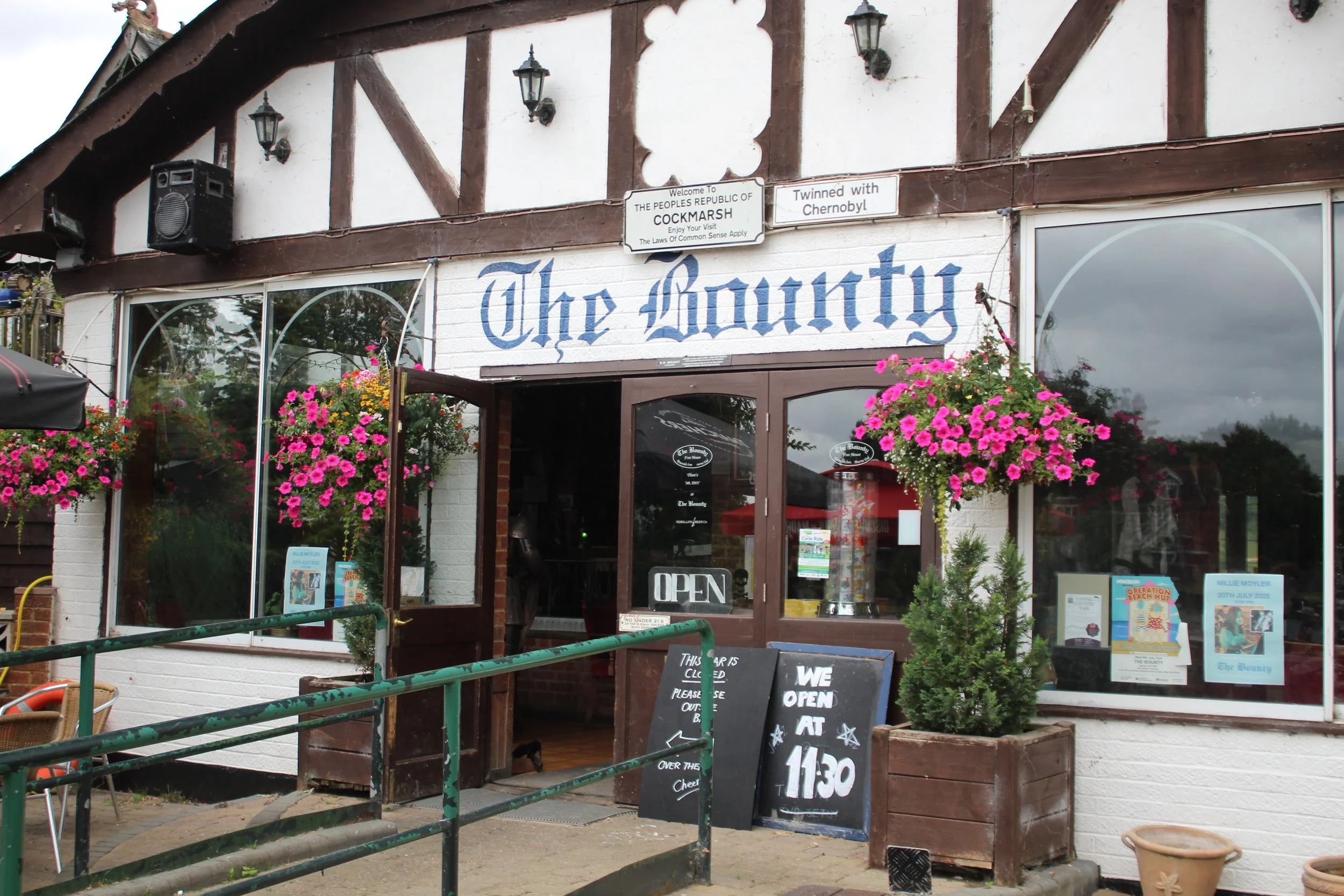 Front view of a restaurant named 'The Bounty' with flower baskets hanging outside, a chalkboard sign, and an 'Open' sign in the window.