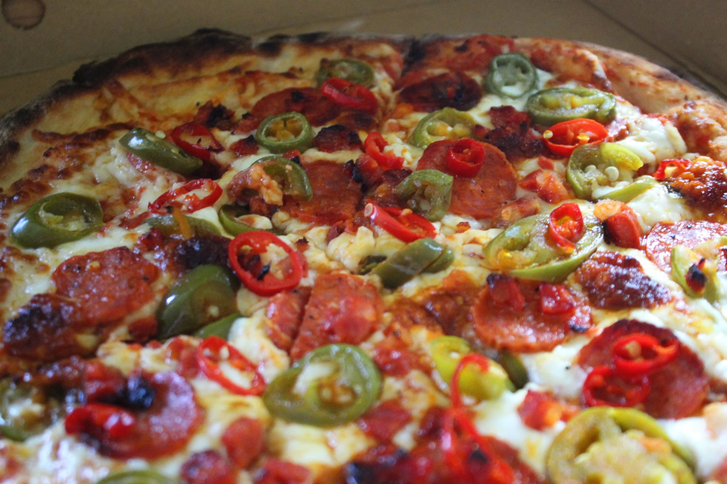 Close-up of a pizza topped with various sliced peppers, sausage, pepperoni, and melted cheese.