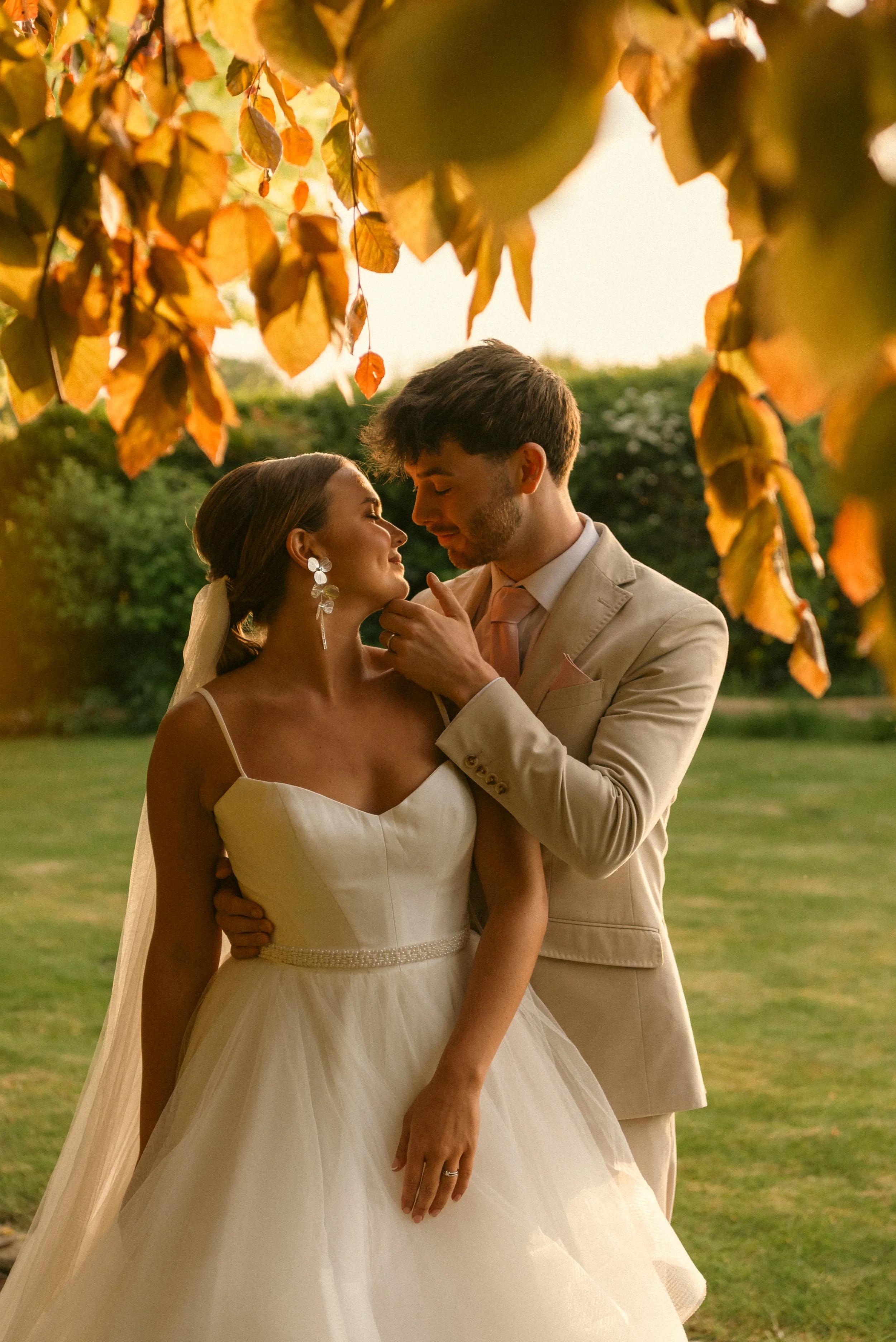 A bride and groom sharing an intimate moment outdoors during sunset, framed by autumn leaves. Styled shoot held at The Cheshire Venue planned by wedding planner Bootique Weddings and Events.