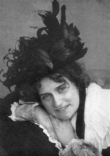 A woman with dark, curly hair lying on her side, resting her head on her hand, smiling at the camera.