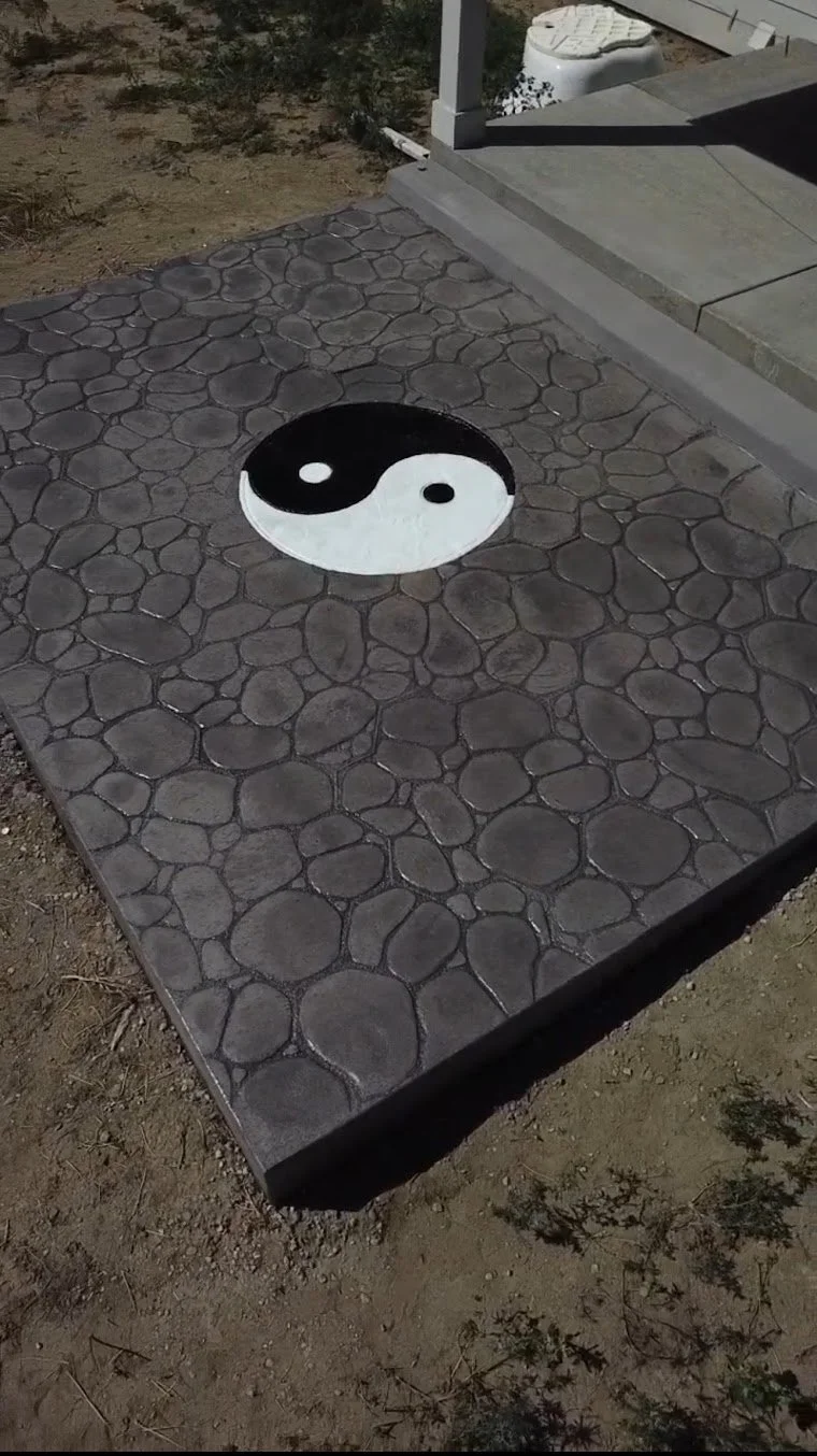 A yin-yang symbol painted on a stone-patterned concrete surface outdoors.