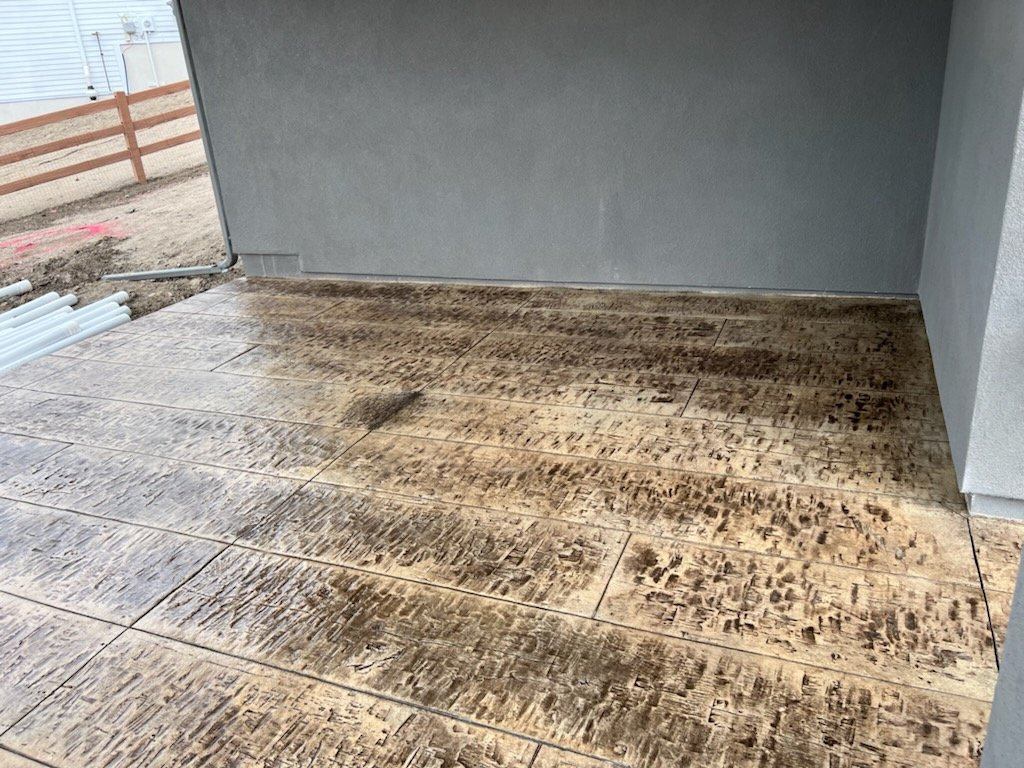 A wooden porch or deck that appears to be stained or charred, likely from a recent cleaning or treatment, situated outside a building with a gray wall.