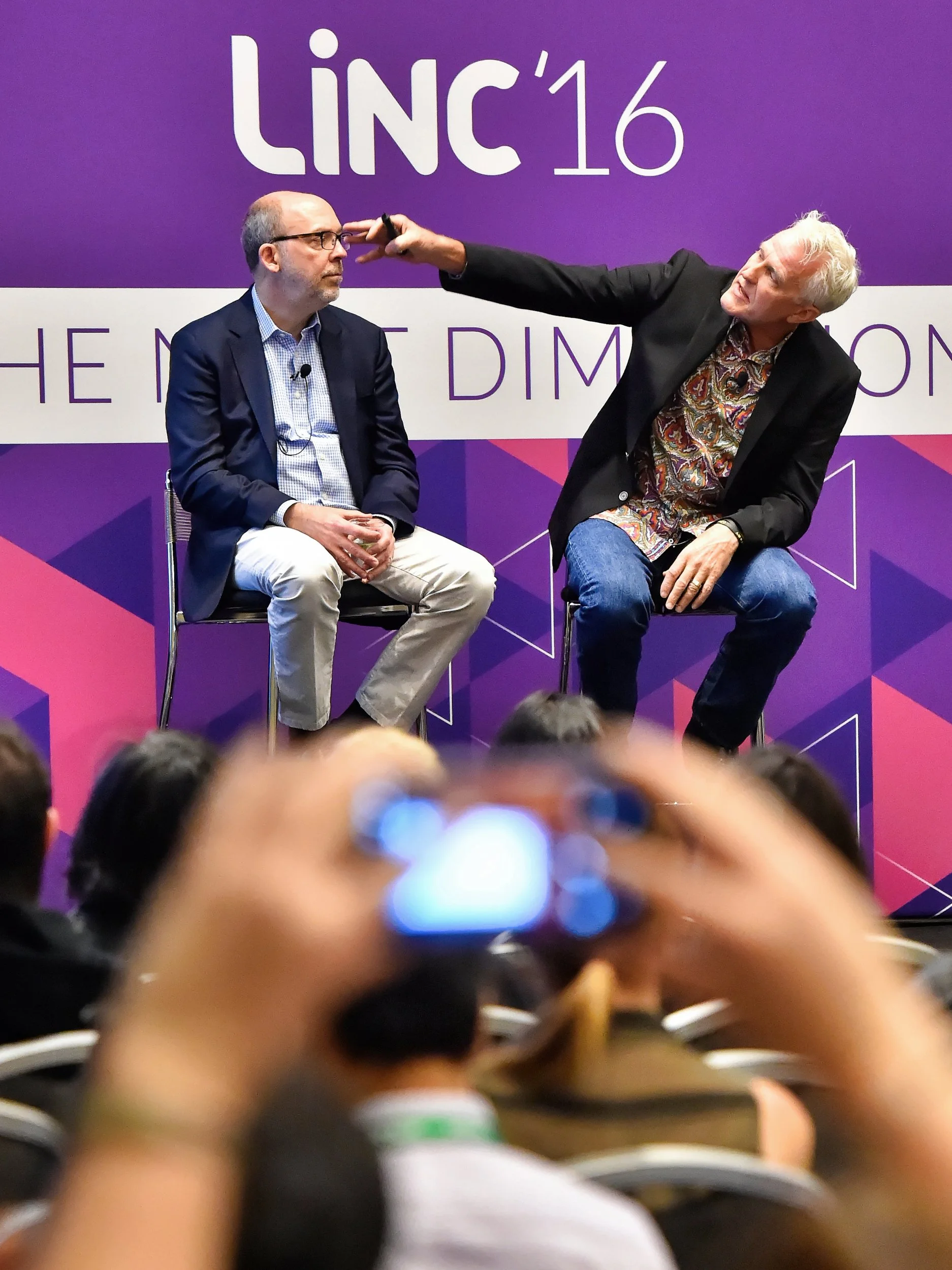Deux hommes en train de discuter lors d'une conférence, avec un fond violet portant le texte 'LINC'16'.