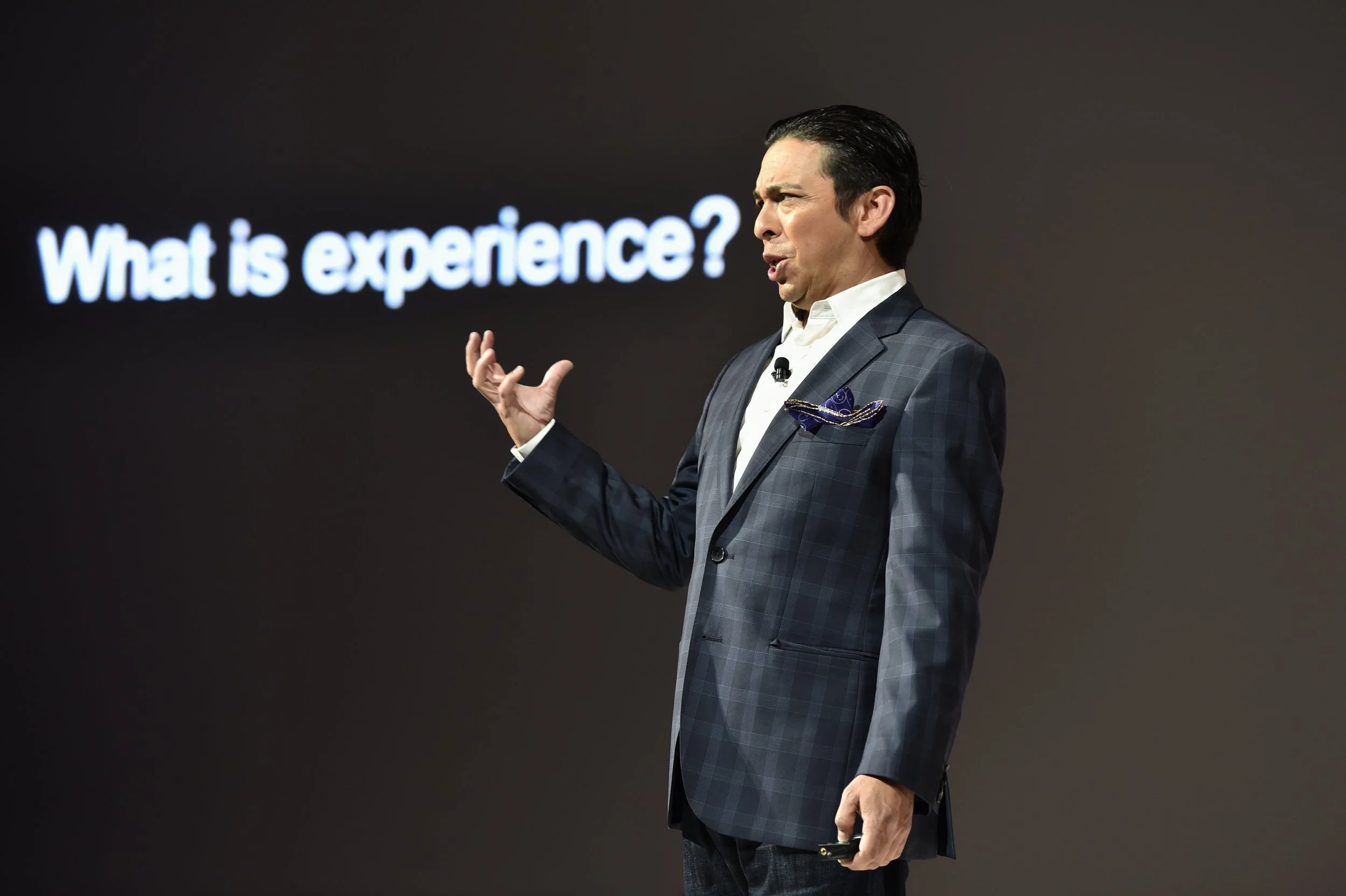 Un homme en costume donne une présentation devant un écran affichant la question "What is experience ?".