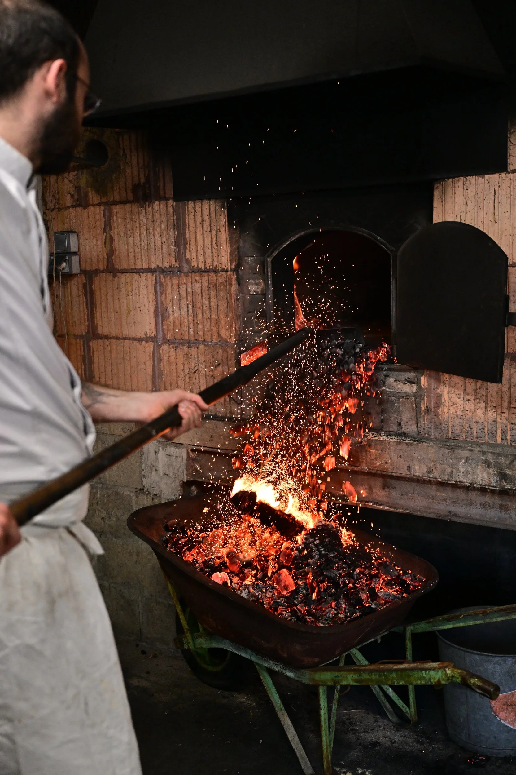 Un forgeron marte un métal chaud dans un grand chaudron en train de produire des étincelles dans une forge.