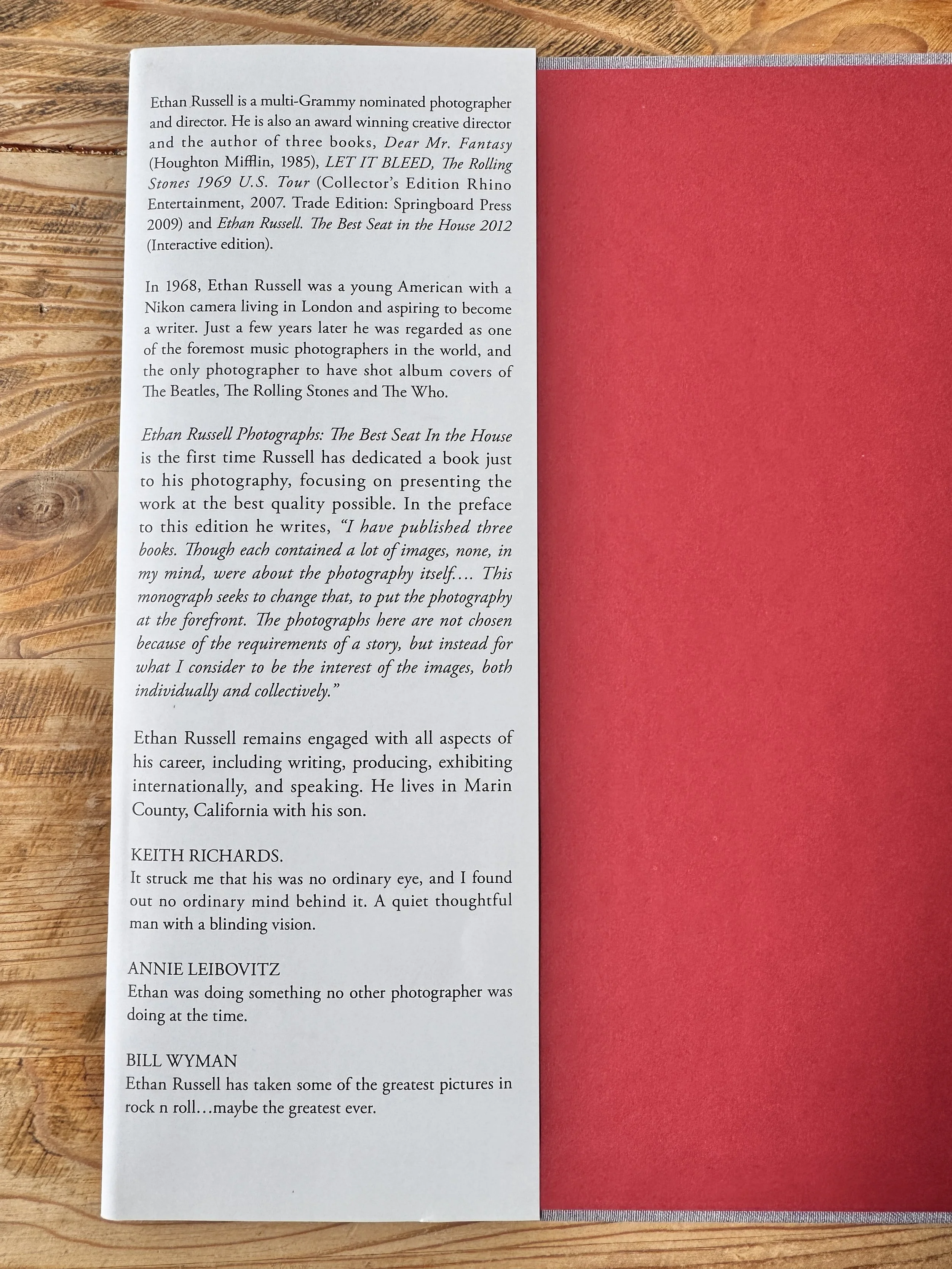 Page de texte d'un livre à gauche et une couverture rouge à droite, posé sur une table en bois.