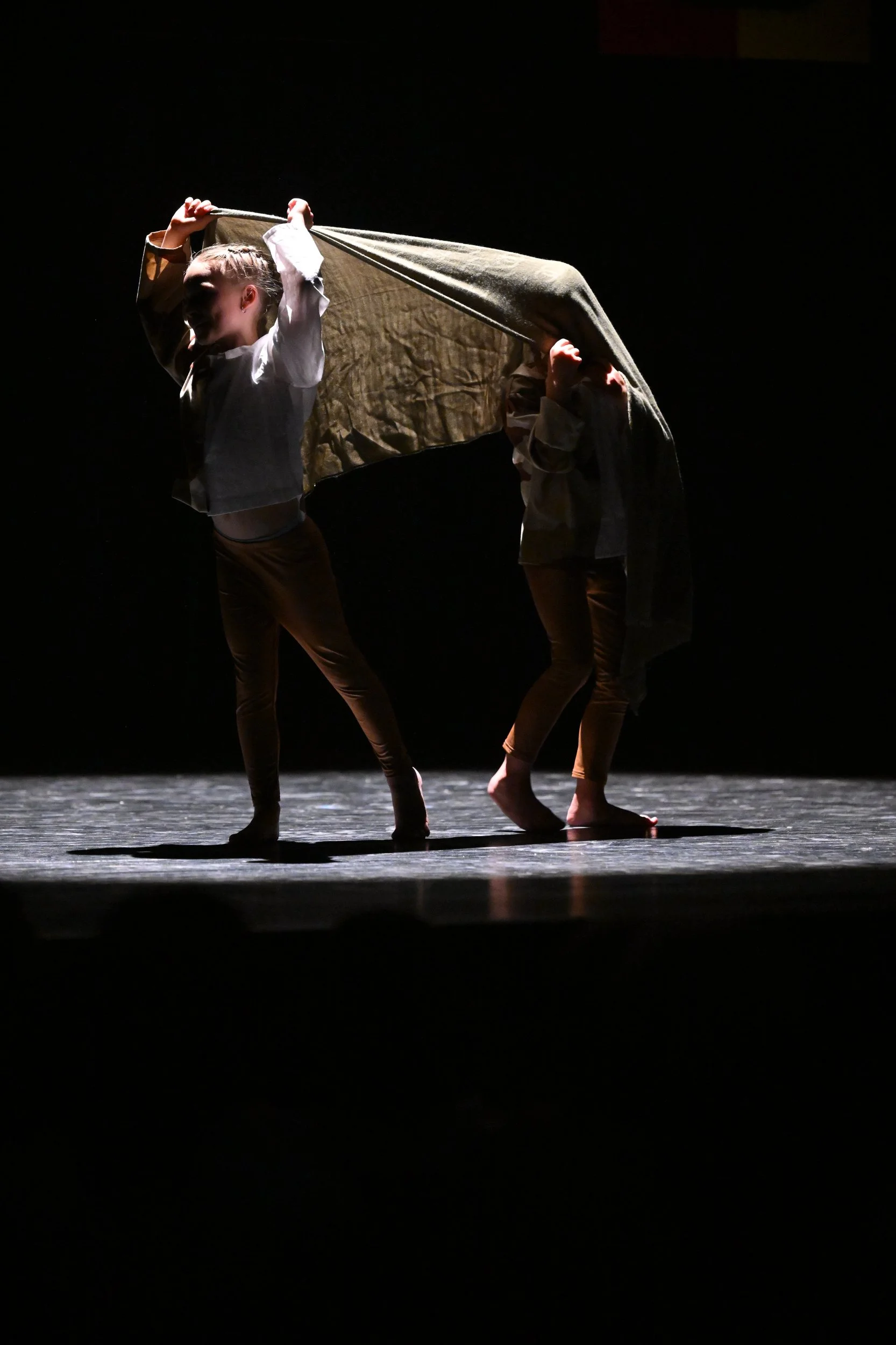 deux danseurs seniors en costume sur scène dans une pièce dramatique, avec un éclairage focalisé sur eux et le fond sombre.