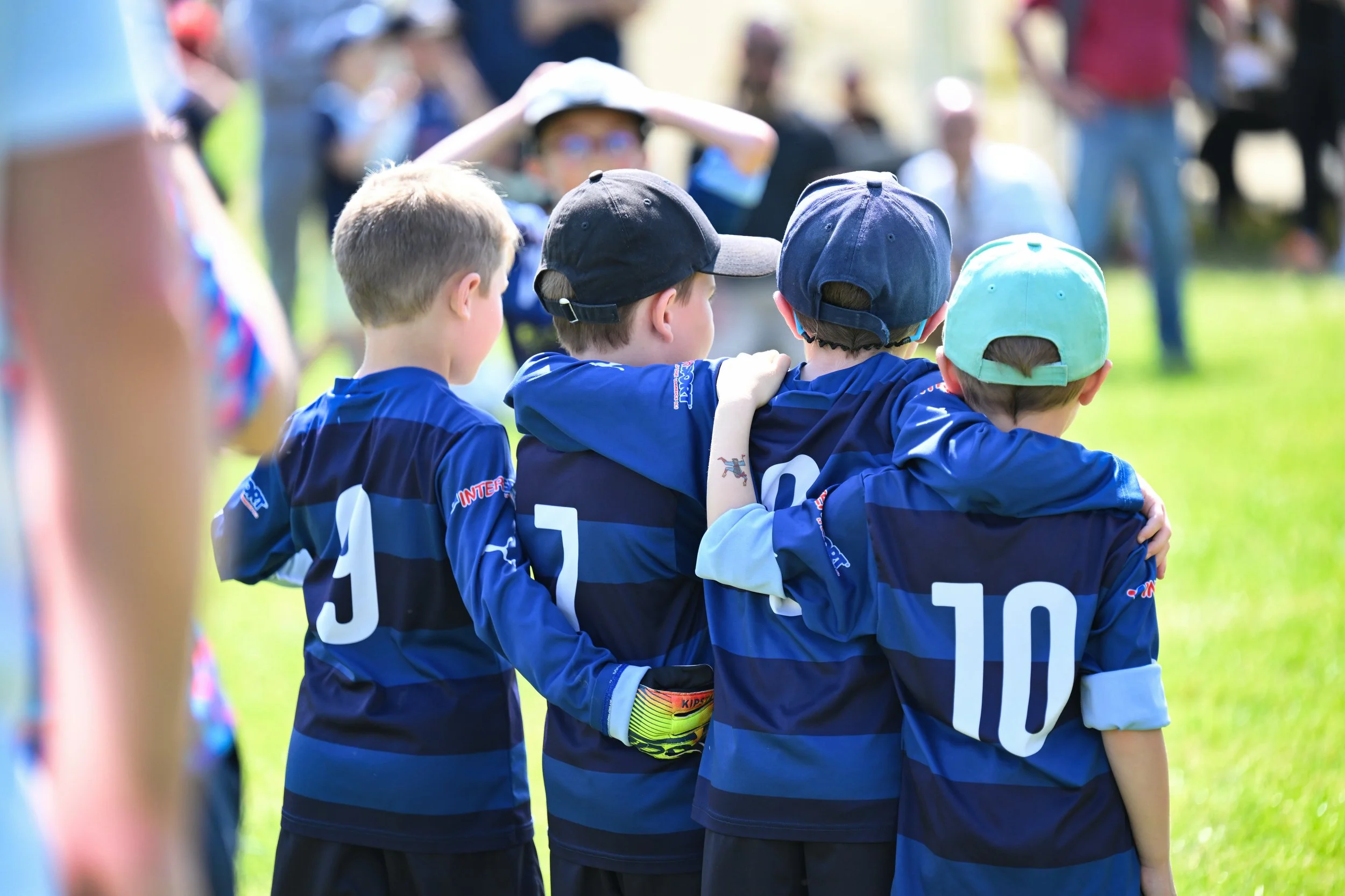 Jeunes joueurs de football en uniforme bleus, avec casquettes, se regroupant lors d'un match ou d'un entraînement en plein air, sous un soleil brillant.