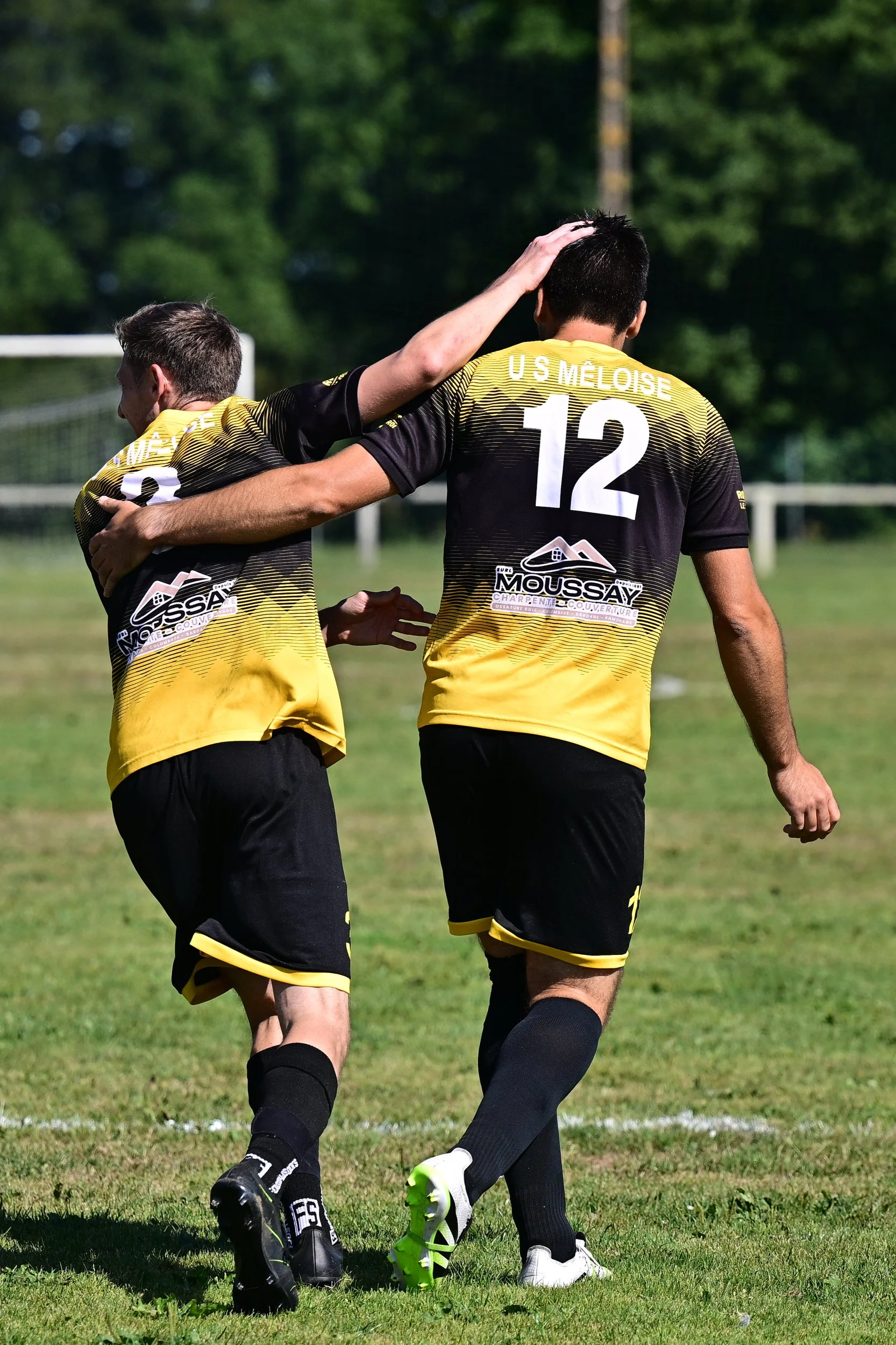 Deux joueurs de football en maillots noirs et jaunes, célébrant sur le terrain, avec une main sur la tête et un bras autour de l'autre.