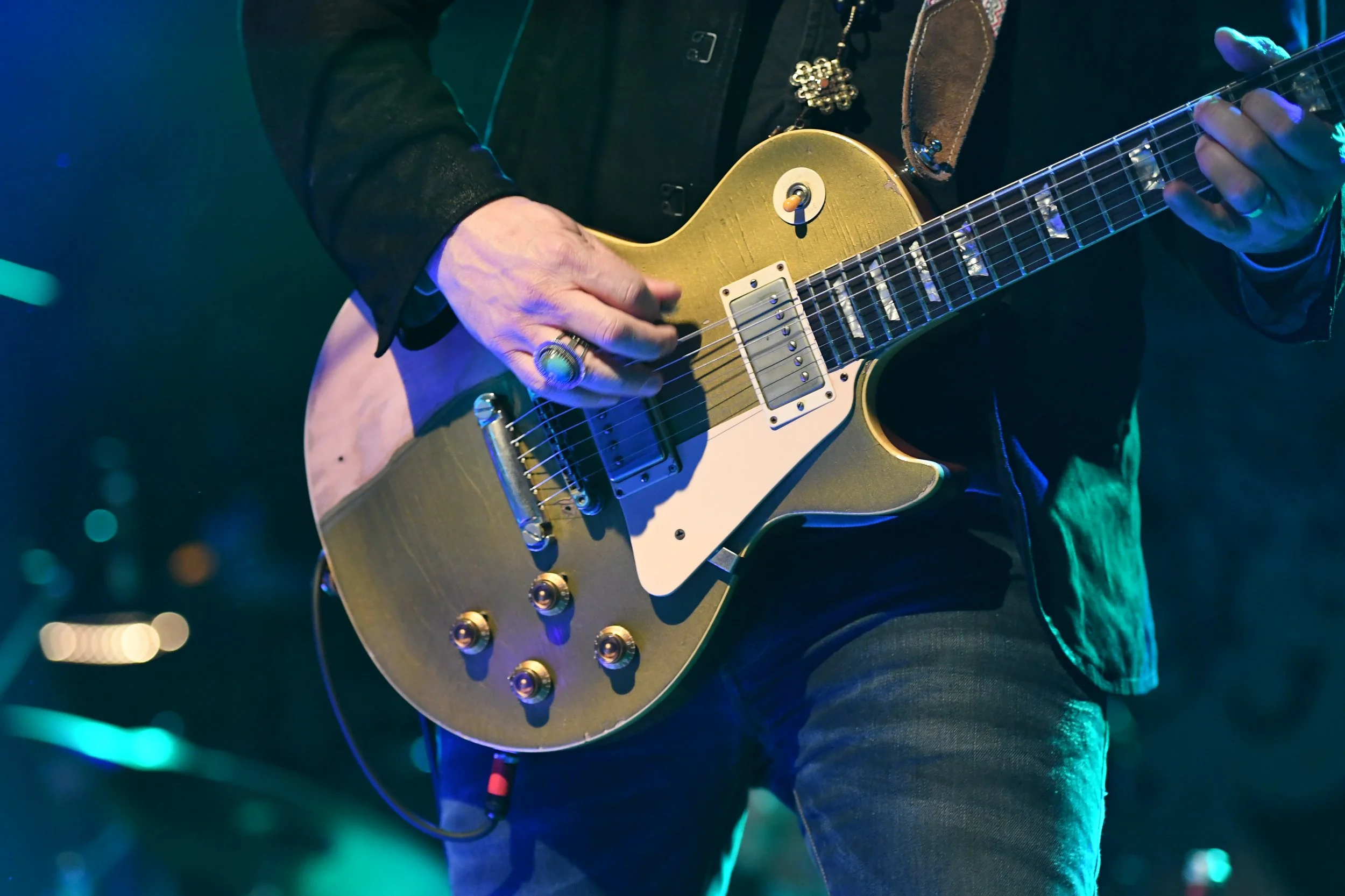 Un musicien joue une guitare électrique dorée, avec des lumières colorées en arrière-plan.