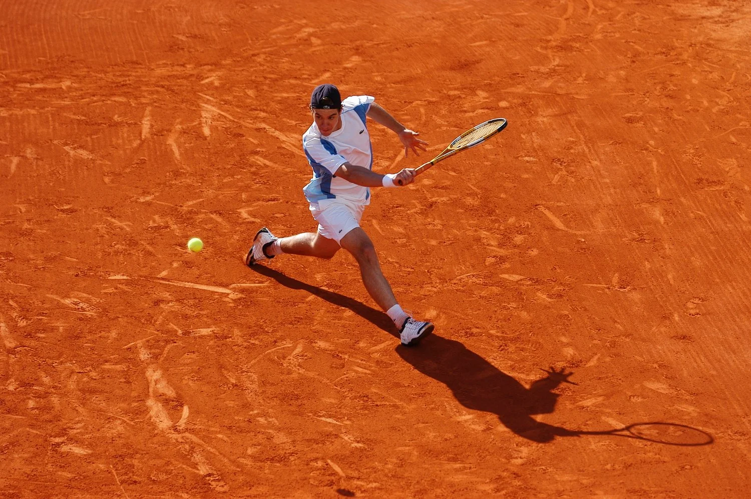 Joueur de tennis en action sur un court en terre battue, préparant à frapper la balle.