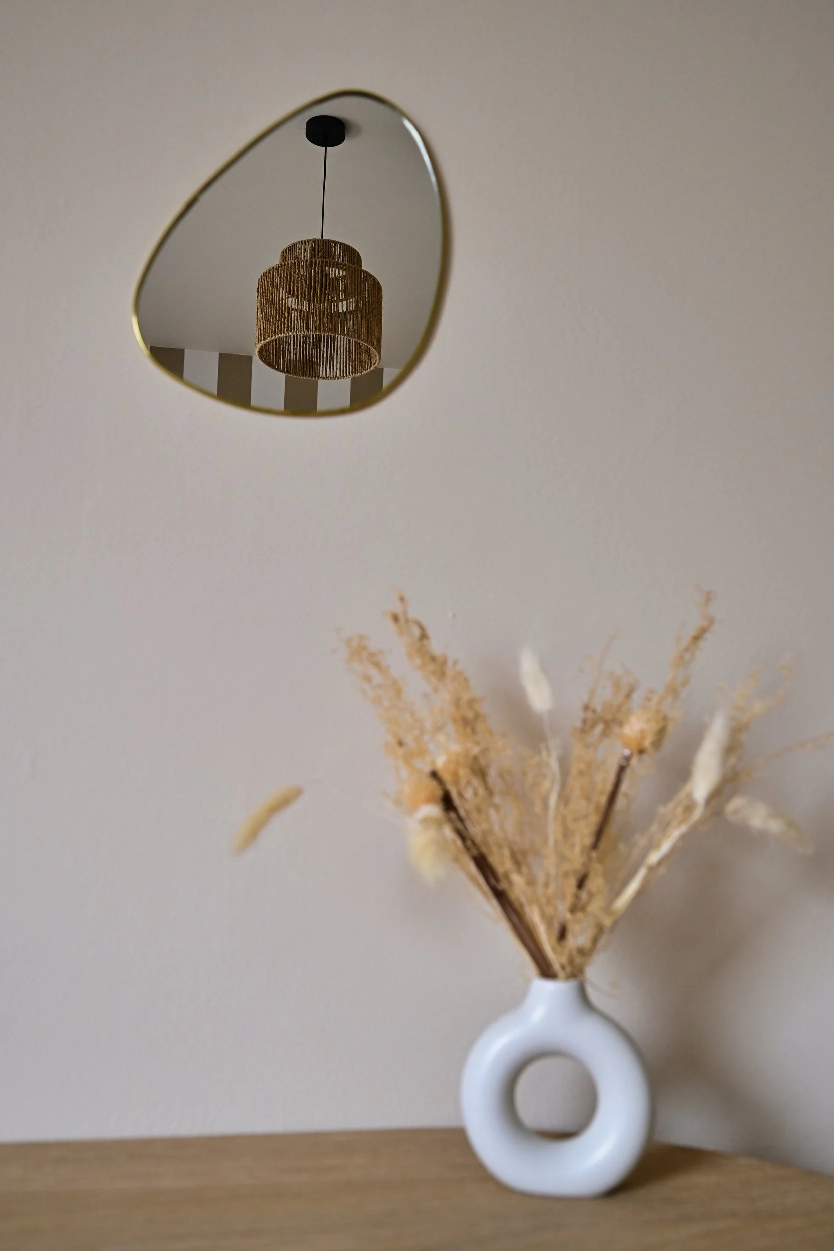 Un vase blanc contenant des branches décoratives et une lampe en miroir au plafond.