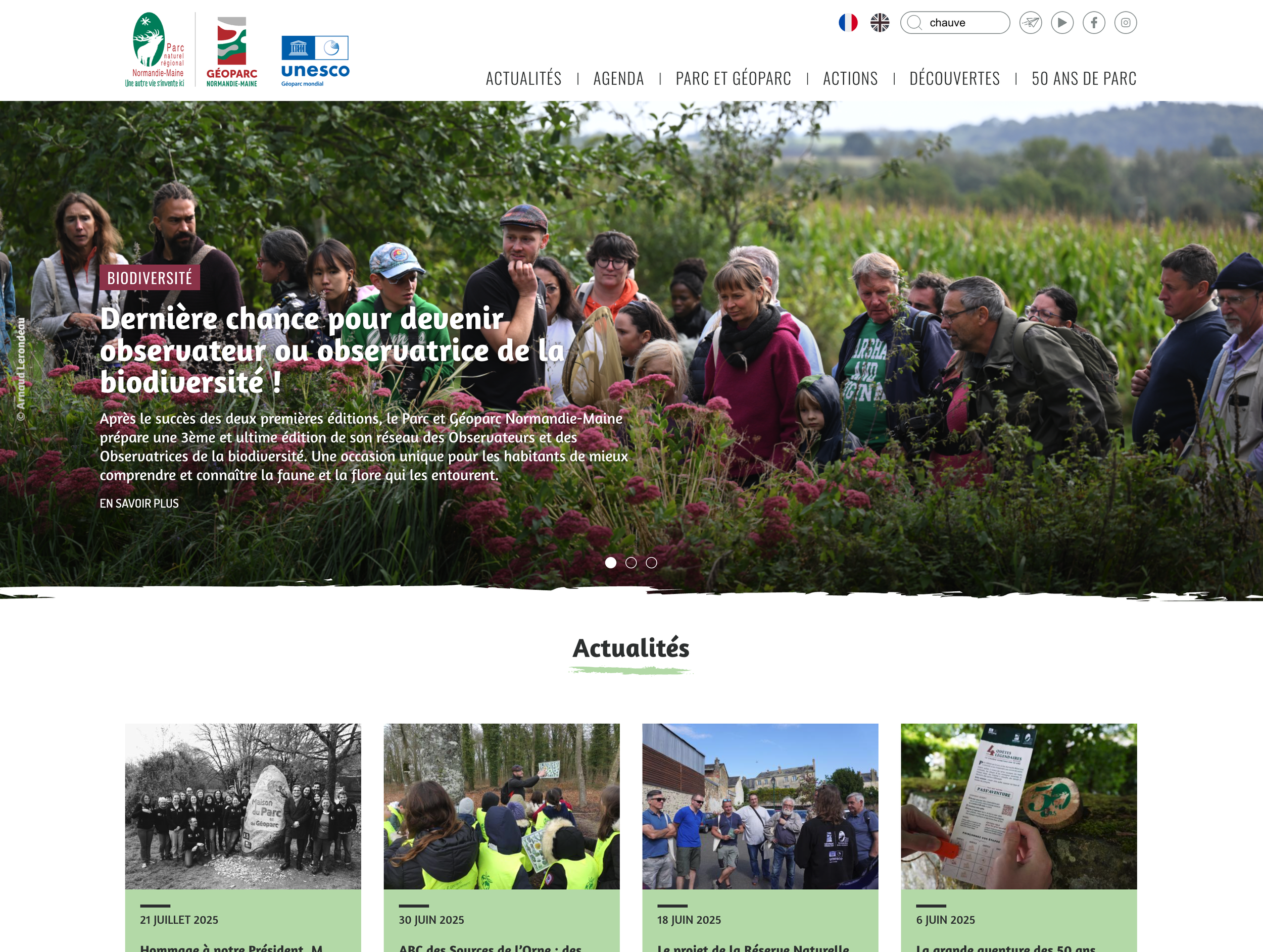 Une foule de personnes lors d'une activité en plein air dans une zone boisée, probablement dans un parc naturel ou une réserve. Des individus regardent une présentation ou discutent, certains portent des chapeaux ou des vestes. L'environnement est ve