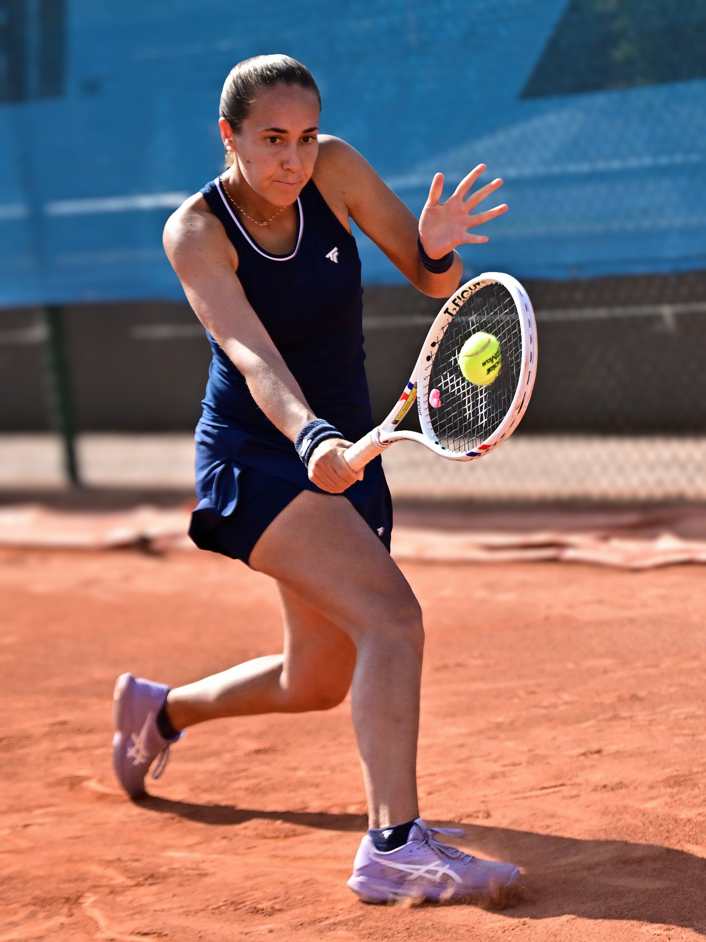 Une femme joue au tennis sur court en terre battue, en train d'effectuer un coup avec sa raquette.