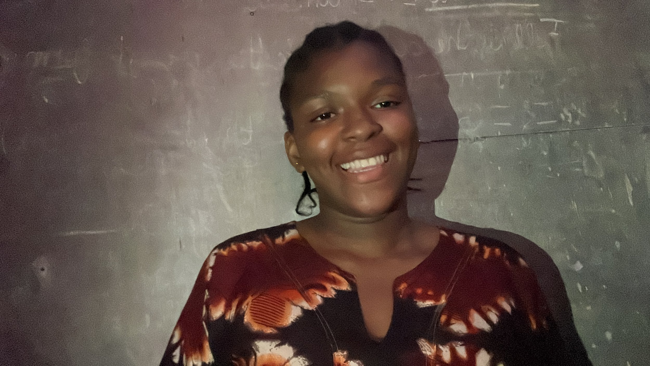 Smiling young woman with braided hair against a dark, scratchy background.