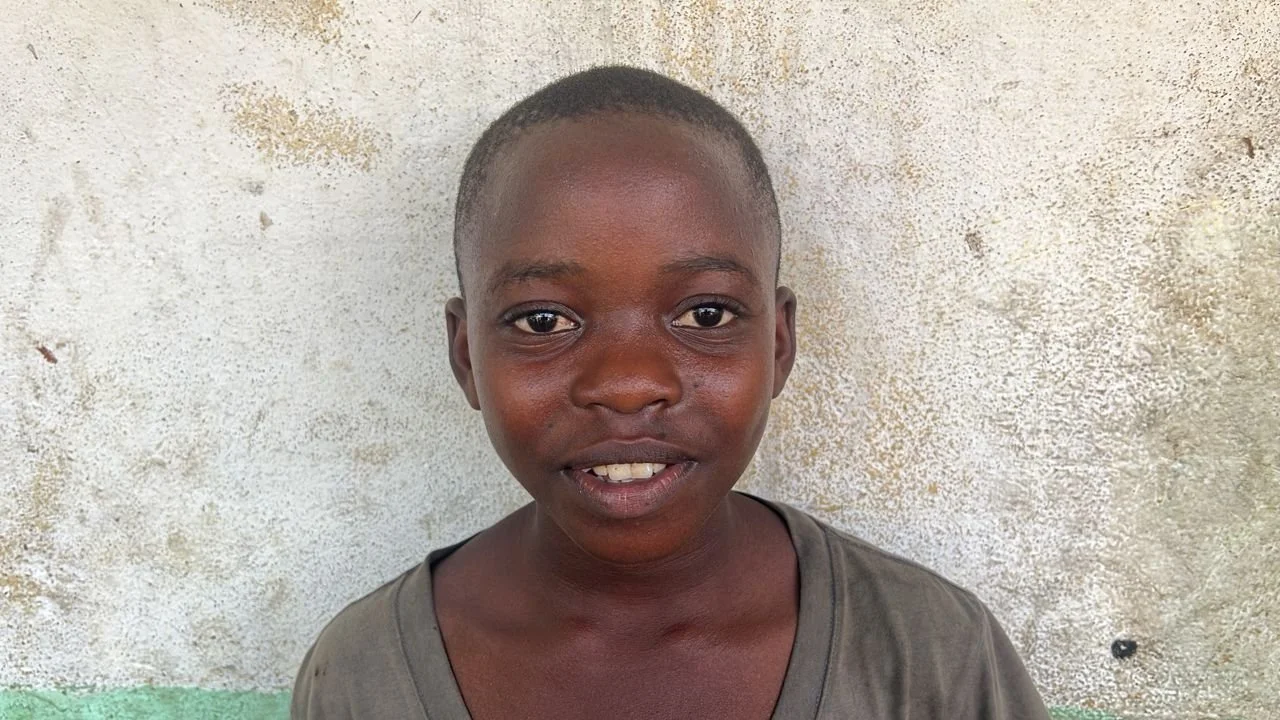 A young boy with dark skin and short hair standing in front of a textured wall.