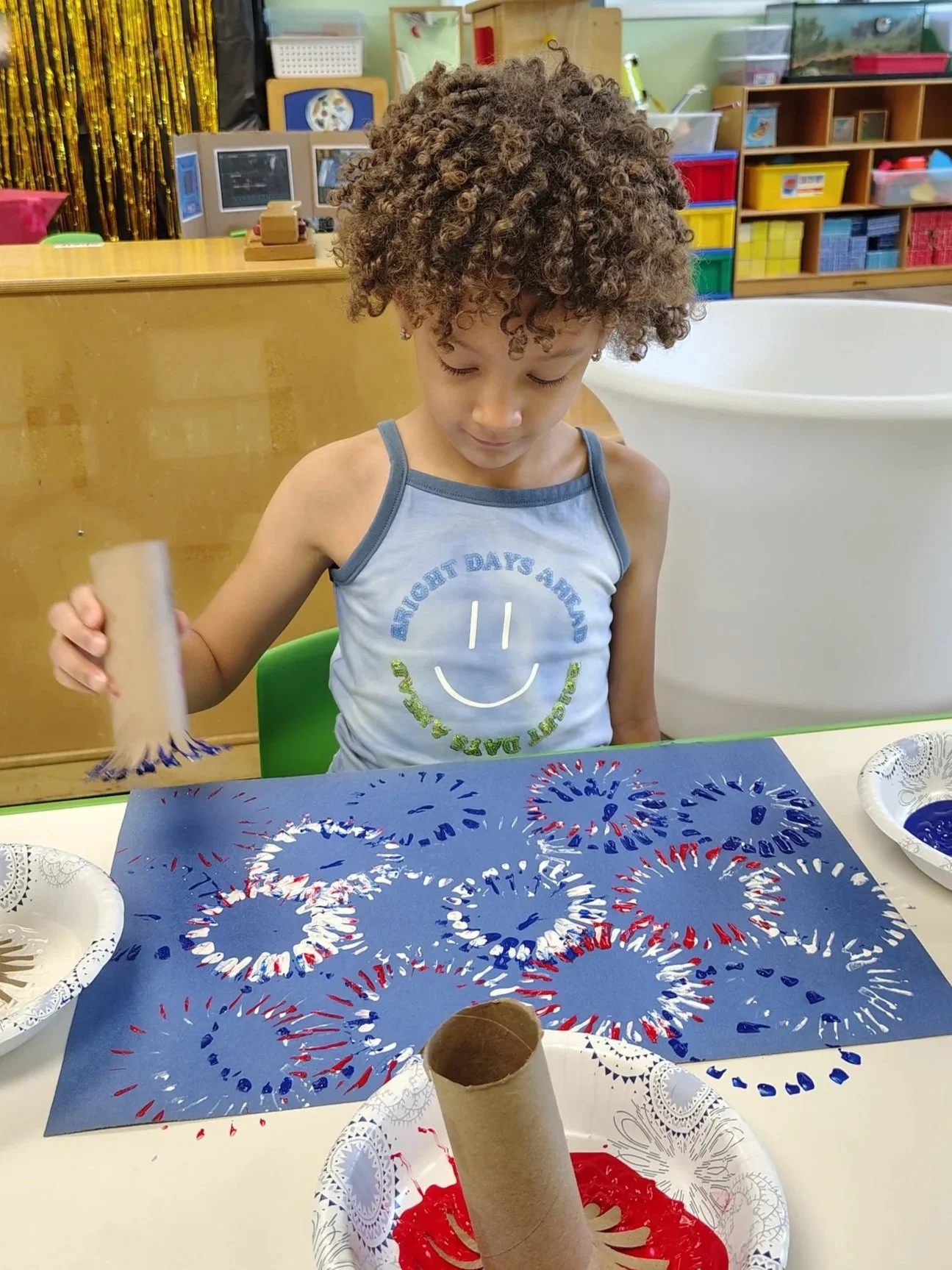 Fireworks craft project with red, white, and blue paint, surrounded by paper towel rolls.