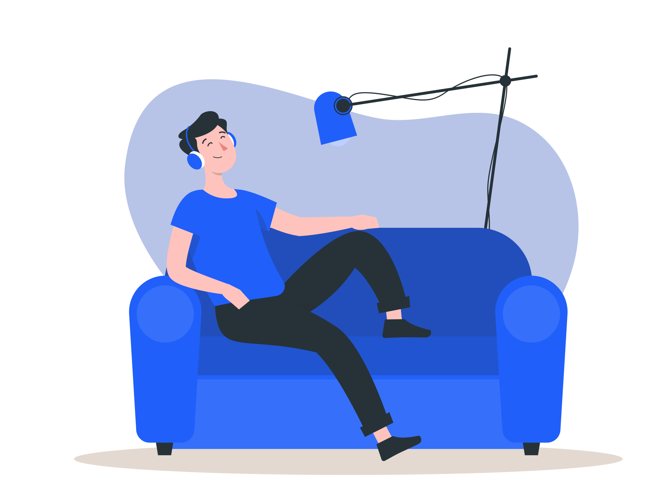 A person sitting comfortably on a blue couch, wearing headphones, with a microphone hanging from a stand above, suggesting they are recording or streaming.
