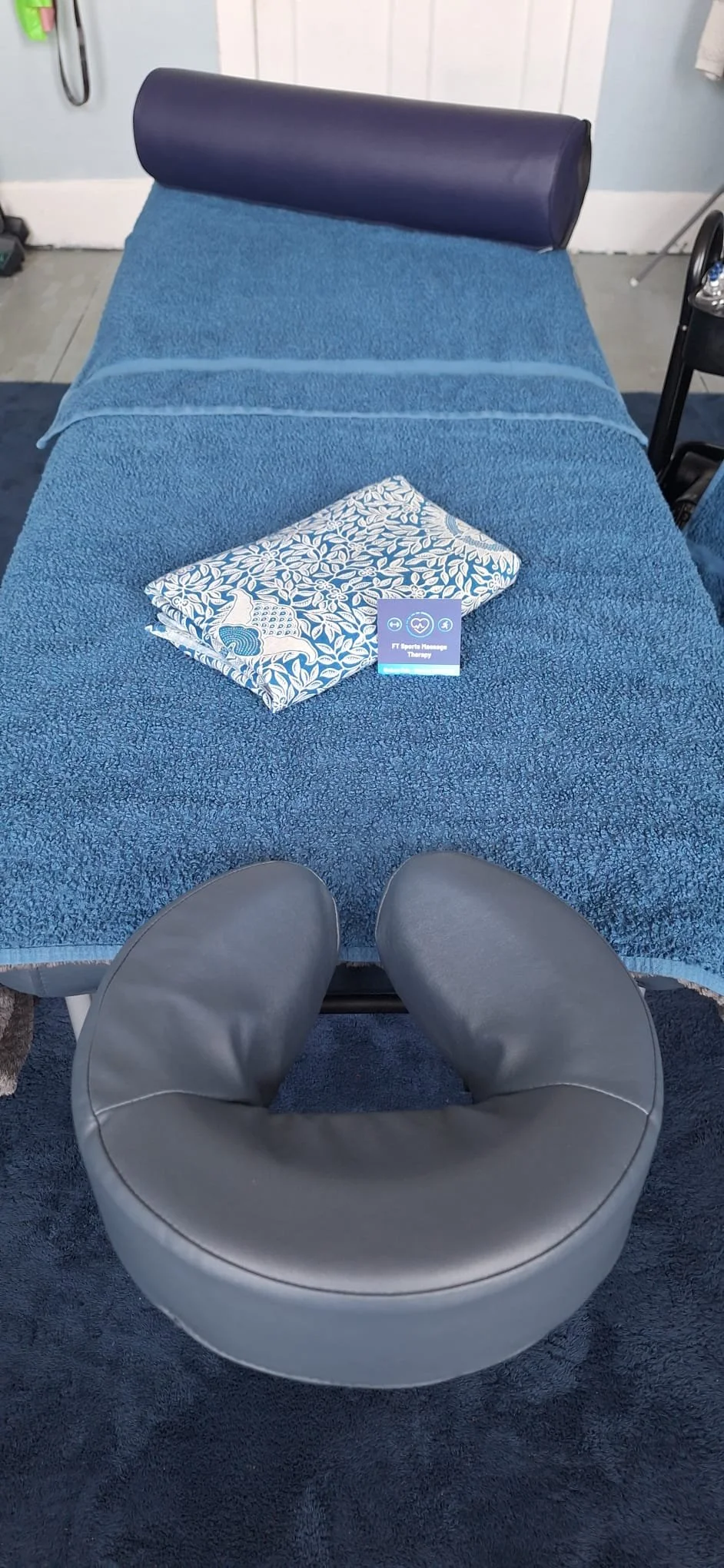 Massage bed made up with blue towels and a business card rested on top